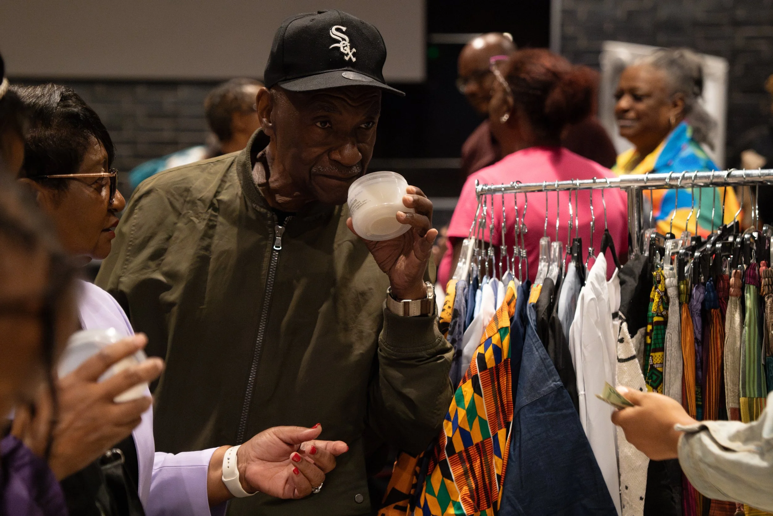 People shopping at a clothing store, looking at colorful garments on a rack, one person sipping from a cup, while others browse or converse.