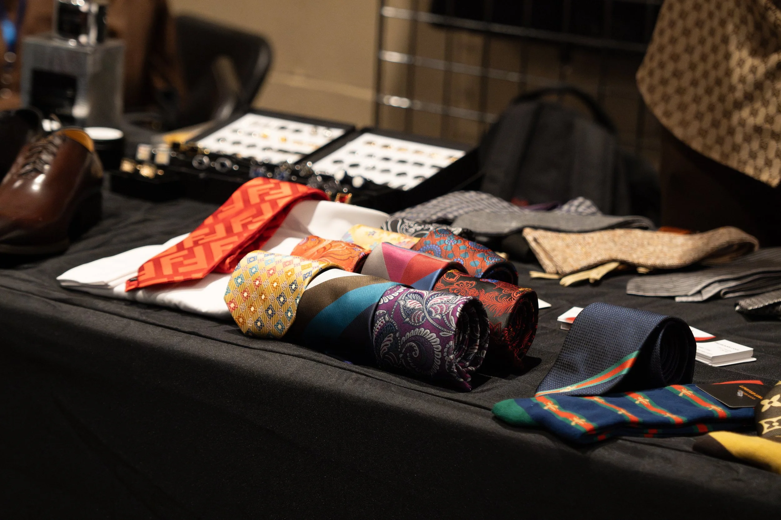 Display of colorful patterned neckties and pocket squares on a black table at an event or sale.