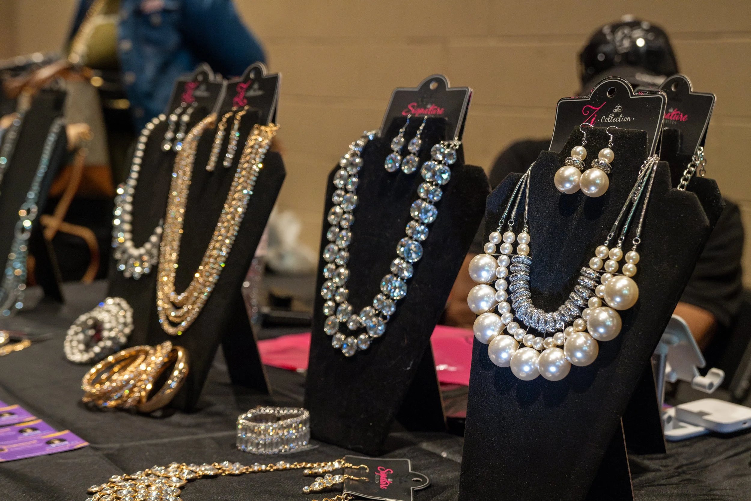 Display of jewelry including various necklaces, earrings, bracelets, and rings on black velvet stands at a retail stall.