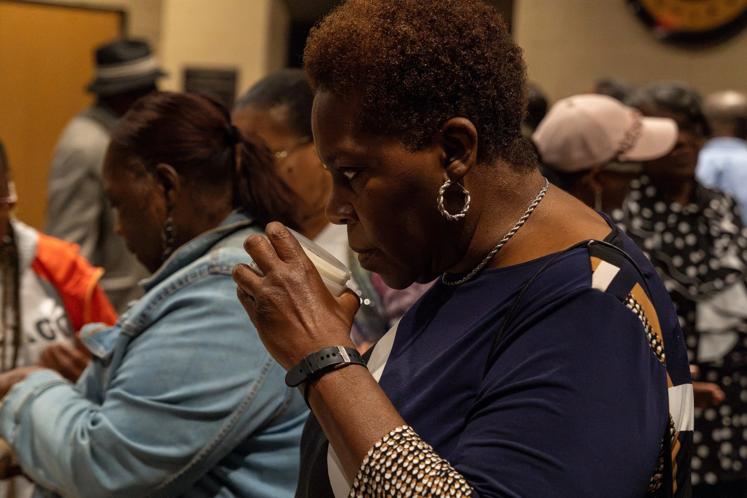 A group of women seated closely together, praying with their heads bowed and hands clasped or holding prayer beads, in what appears to be a religious or spiritual gathering.
