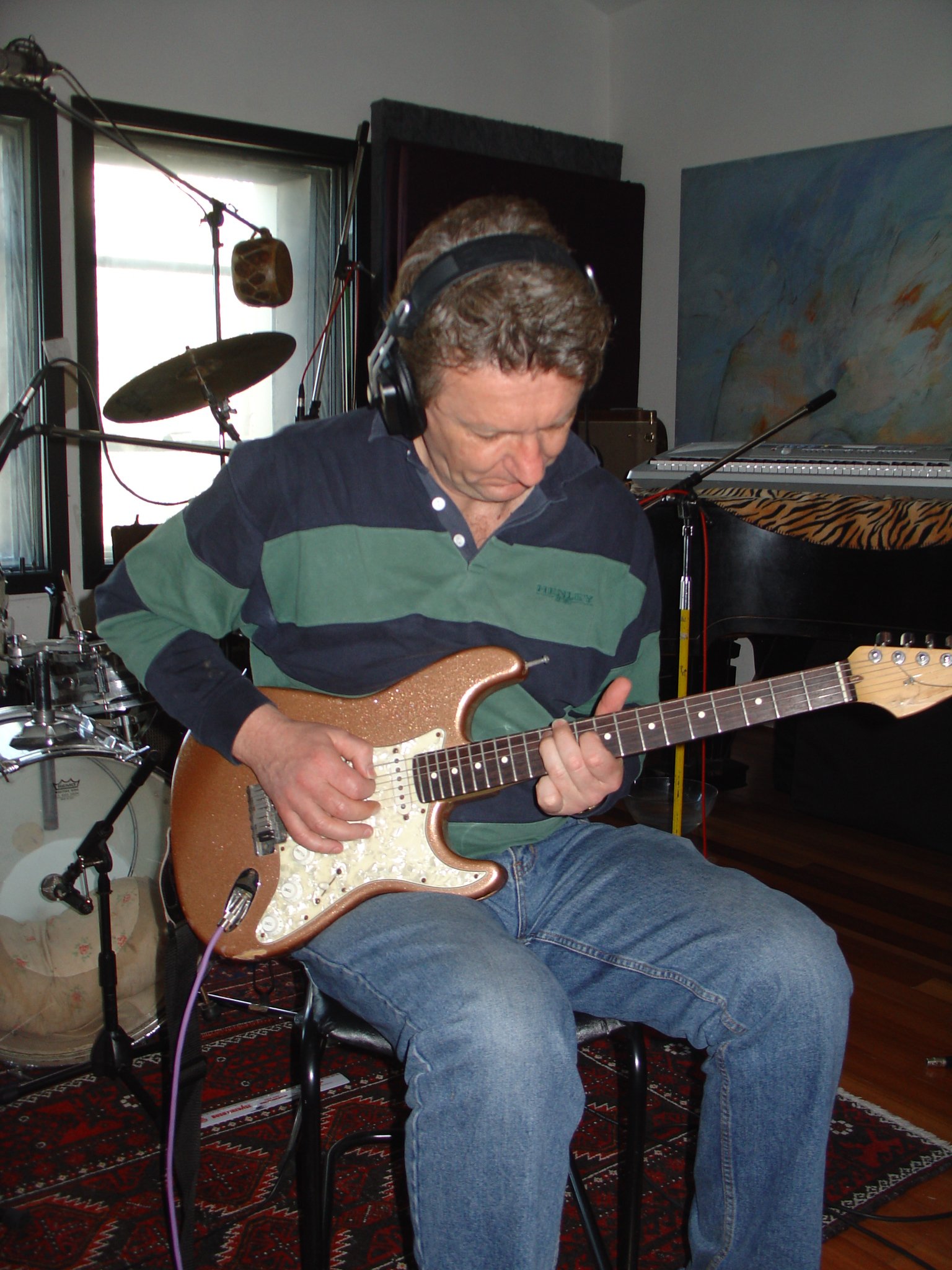 A man wearing headphones playing an electric guitar in a music studio.
