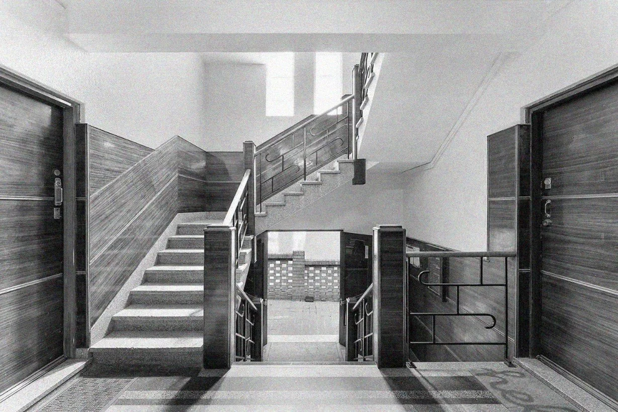 Interior view of a staircase with wooden paneling and metal railings in a building lobby, with closed doors on either side.