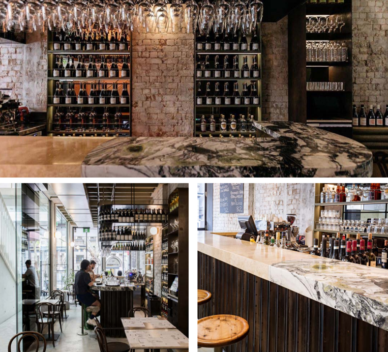 Interior of a bar or restaurant with wine bottles displayed on shelves, a marble countertop, and customers dining.