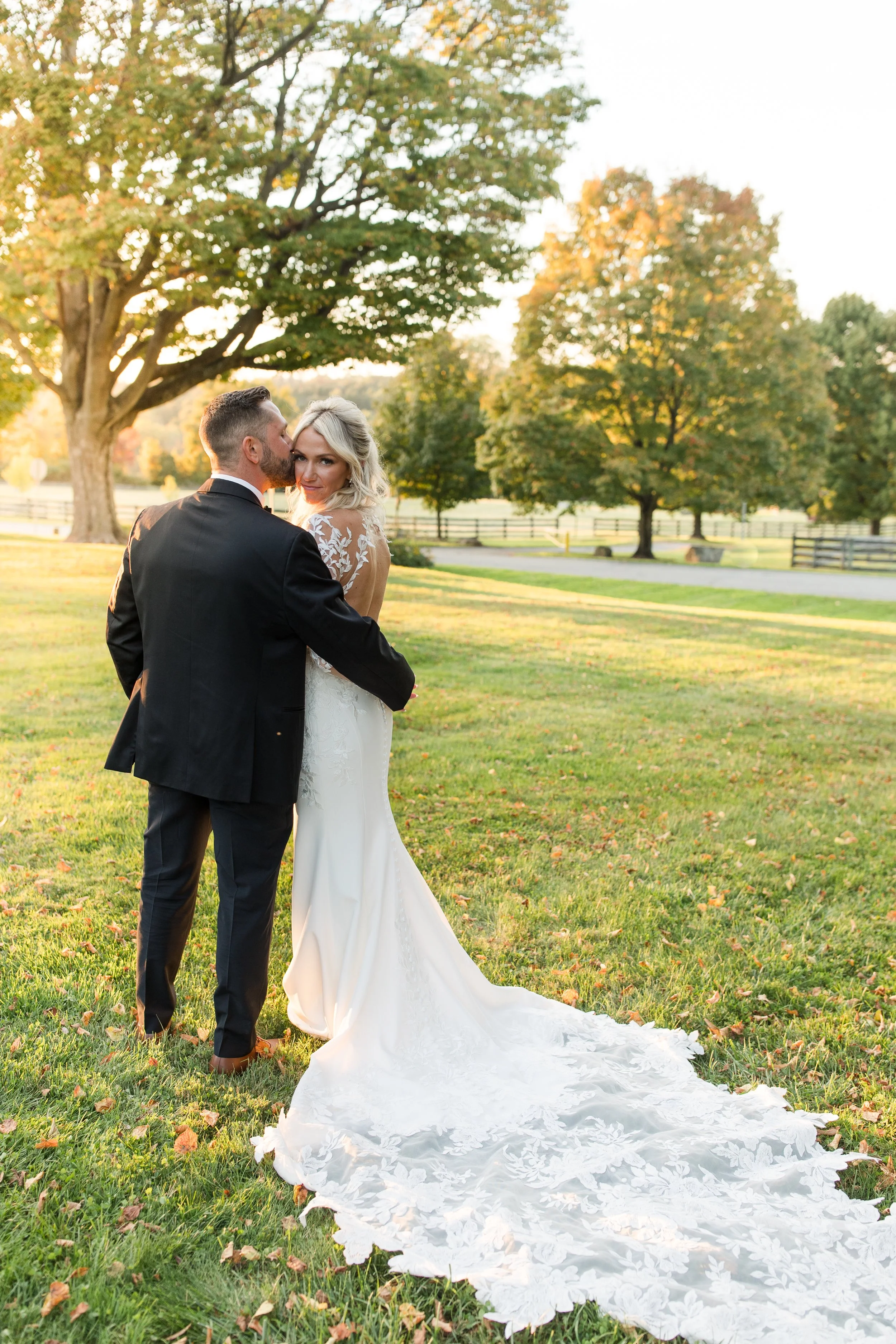 Bride and groom embracing outdoors with the bride's lace train displayed behind her