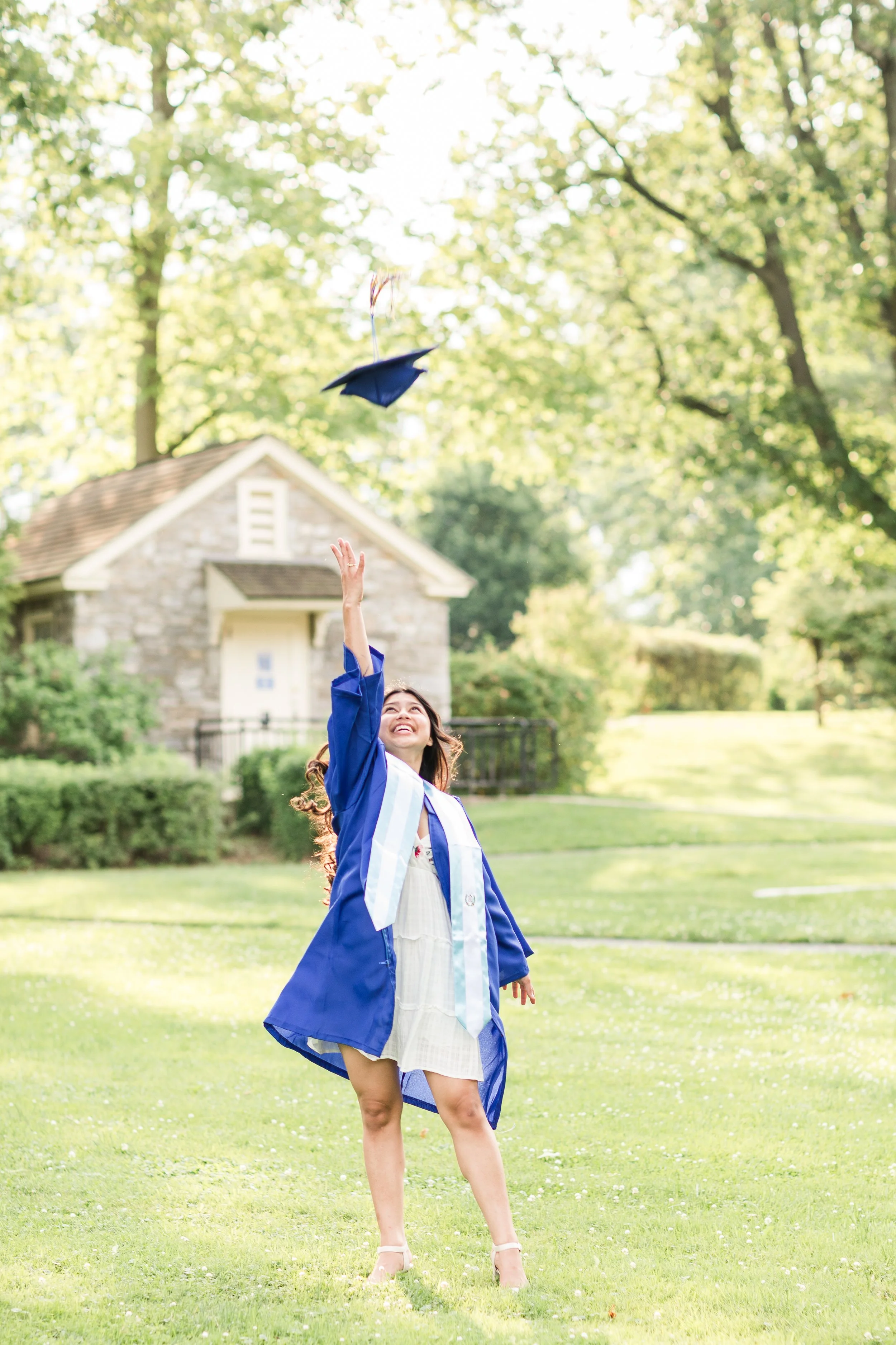 Graduating senior in a blue cap and gown tossing her graduation cap outdoors