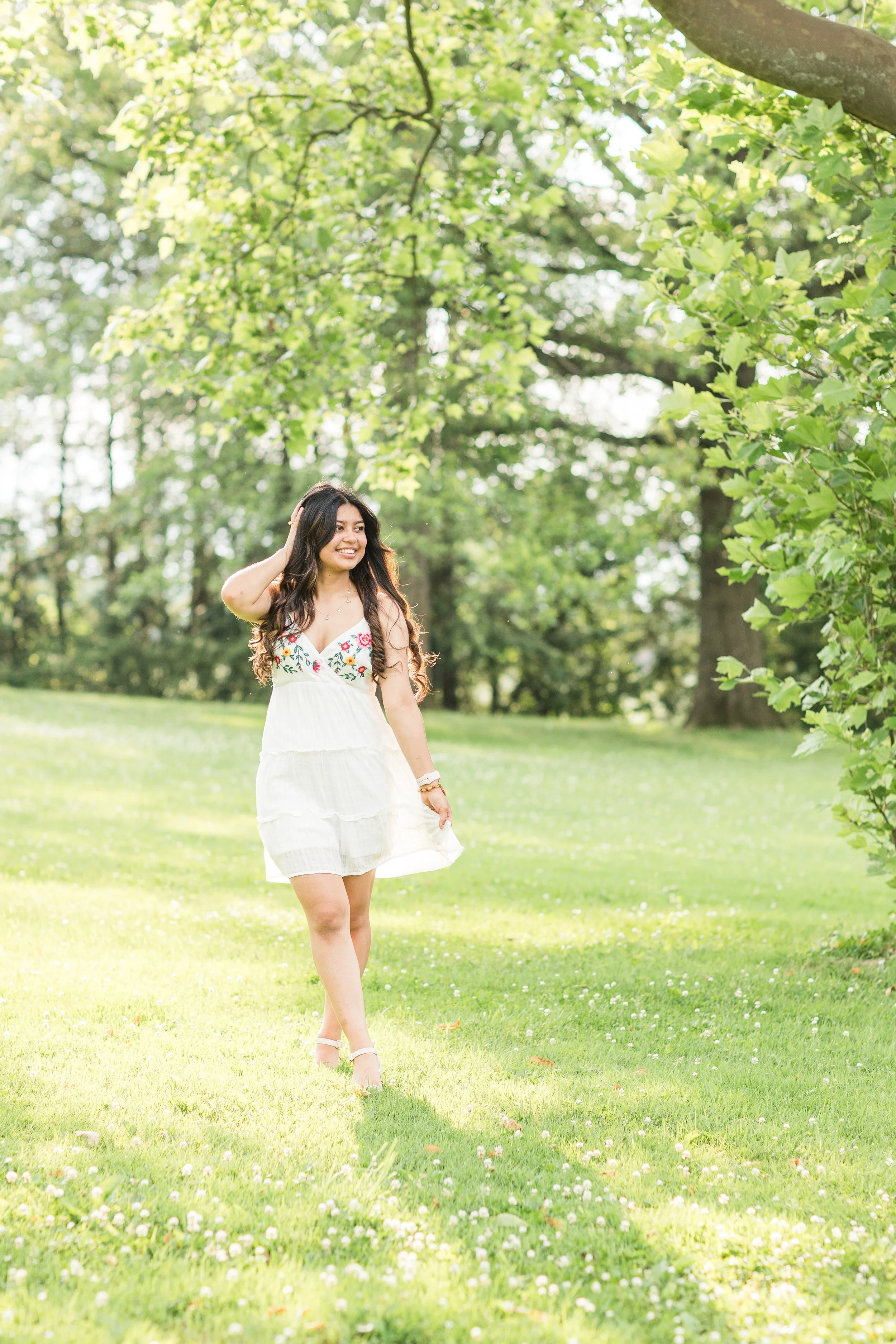 High school senior walking through a sunny green field in a white floral dress