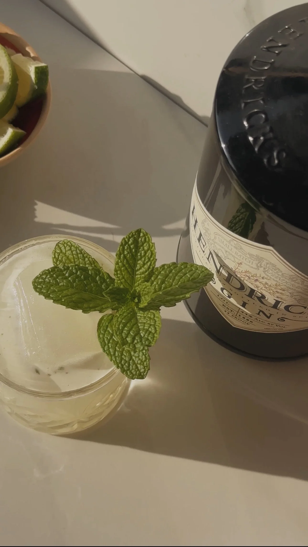 A glass of white beverage garnished with fresh mint leaves, a dark jar labeled "Chandon", and a bowl of lime wedges in the background.
