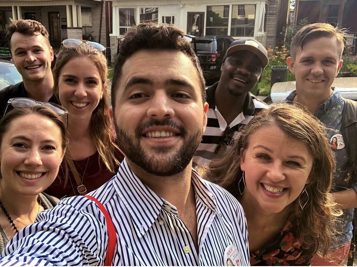 Group of volunteers with Julie Dzerowicz taking a selfie outdoors in a residential neighbourhood. They are smiling and appear happy.