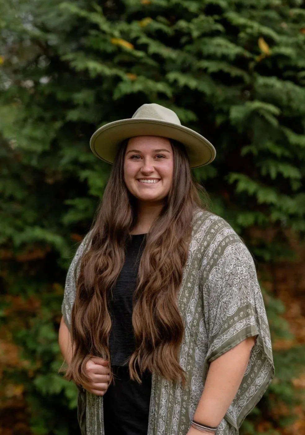 Emily Mulvaine, wearing a green patterned shawl and a green hat with long brown hair and an inviting smile.