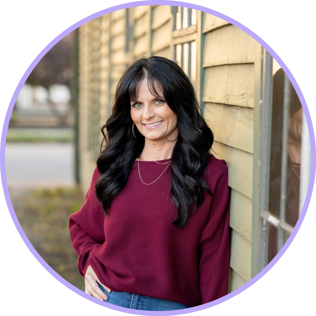 Vanessa Bryan standing next to a building with black hair, a maroon sweater and blue jeans.
