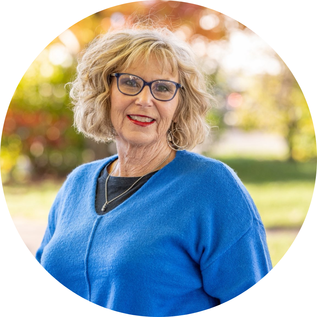 Wendy Ash, wearing a blue sweater with short, blonde hair, glasses, and a warm smile.