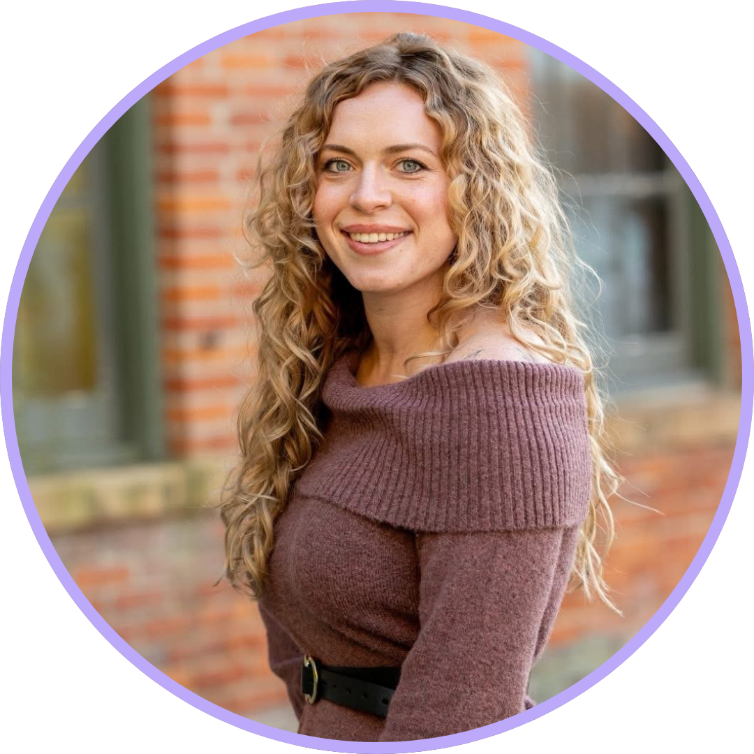 Hannah McMillen wearing a brown sweater dress with blonde curly hair and a bright smile.