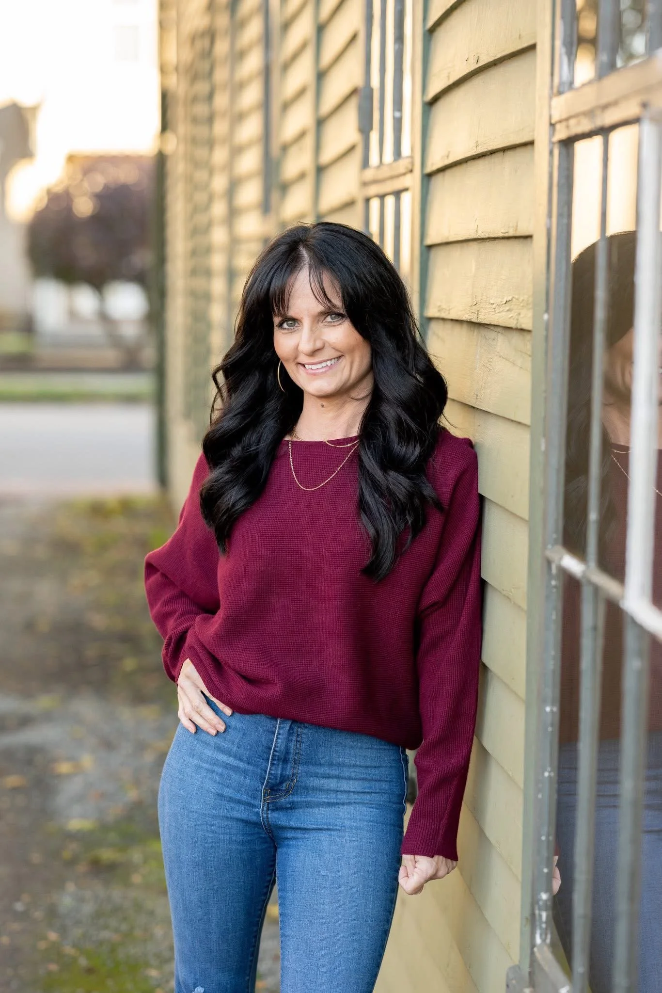 Vanessa Bryan standing next to a building with black hair, a maroon sweater and blue jeans.