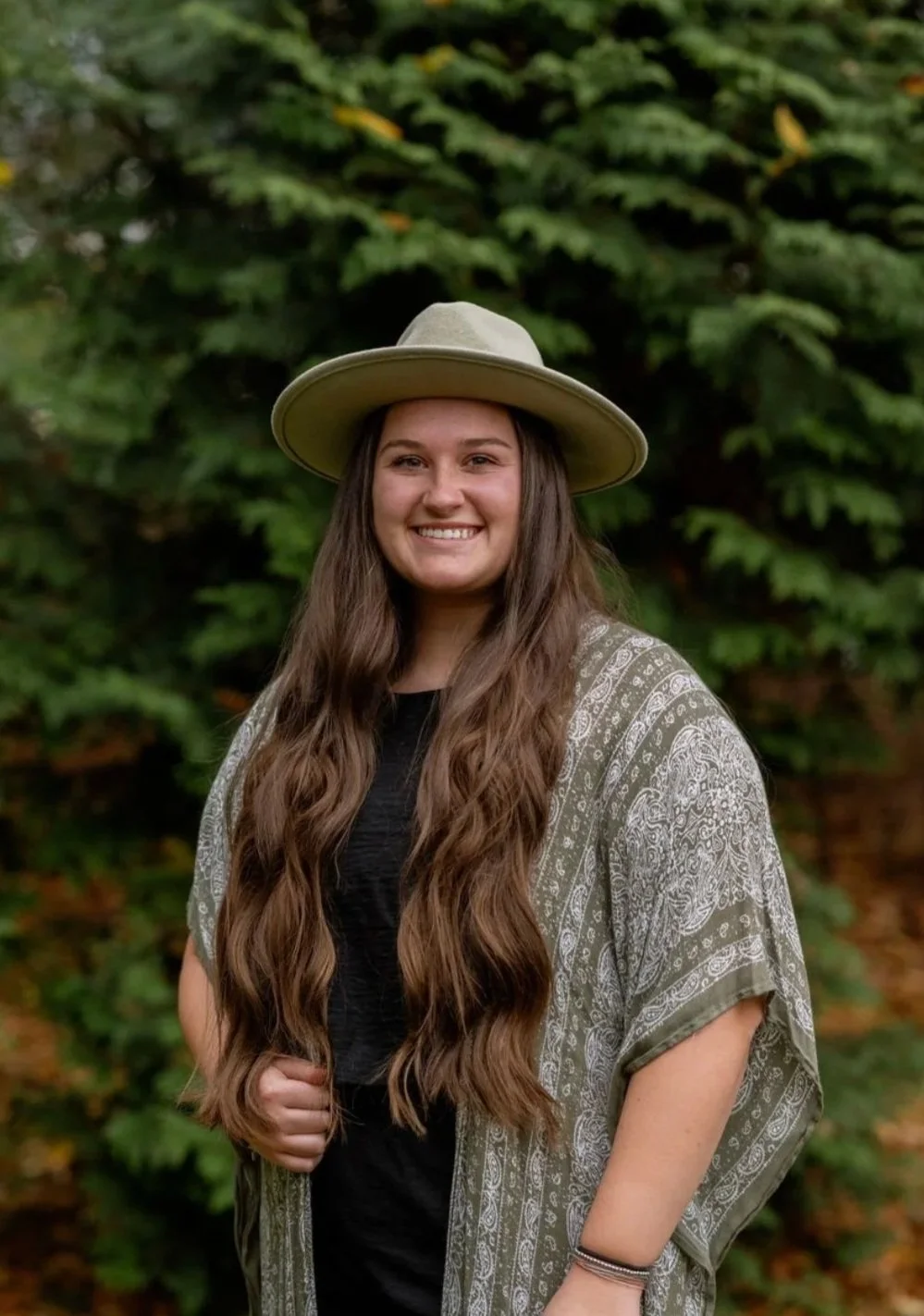 Emily Mulvaine, wearing a green patterned shawl and a green hat with long brown hair and an inviting smile.