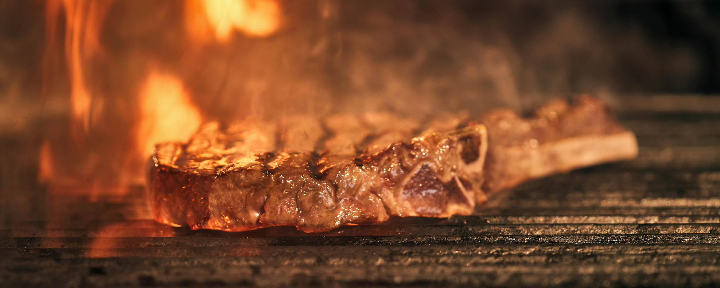 A steak cooking on a grill inside a barbecue or oven with flames visible.