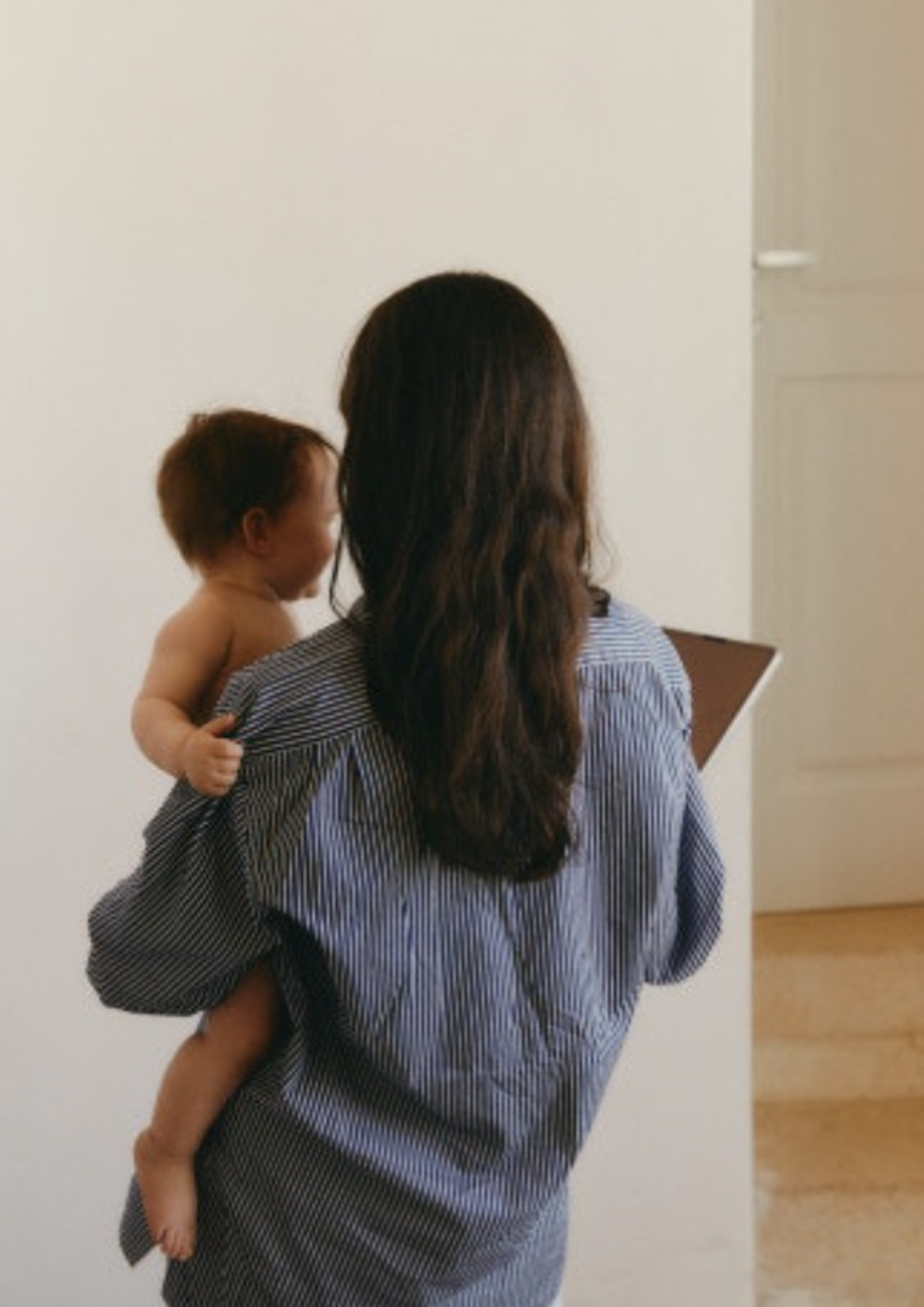 Woman with long dark hair carrying a small toddler in a striped shirt.