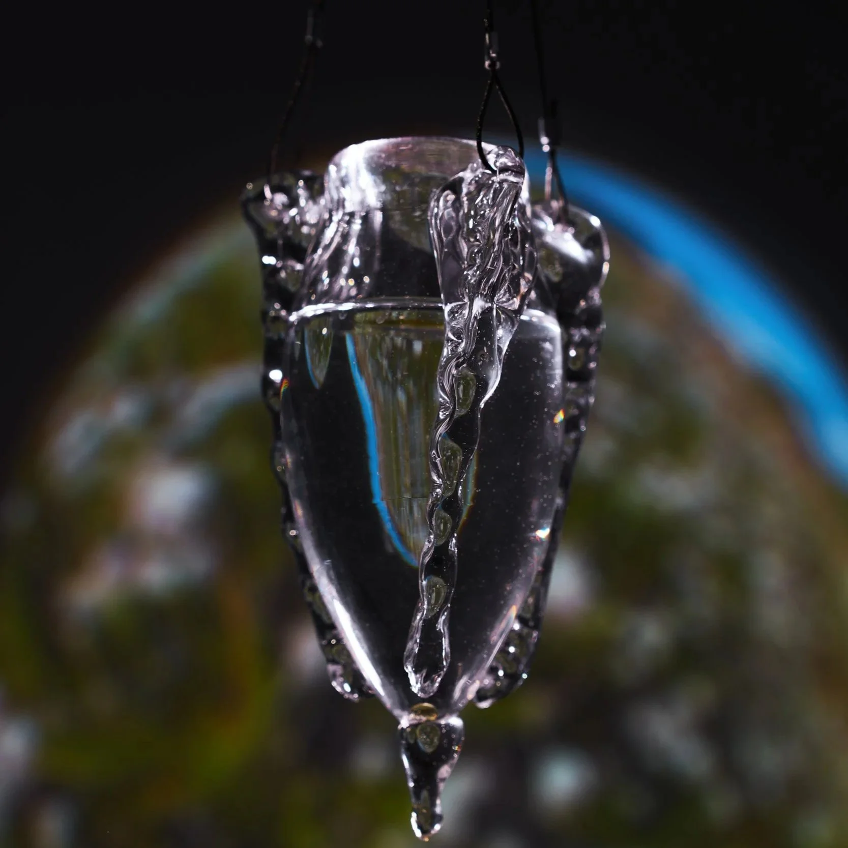 Close-up of melting ice cube hanging with water droplets falling off, with blurred background of Earth from space.