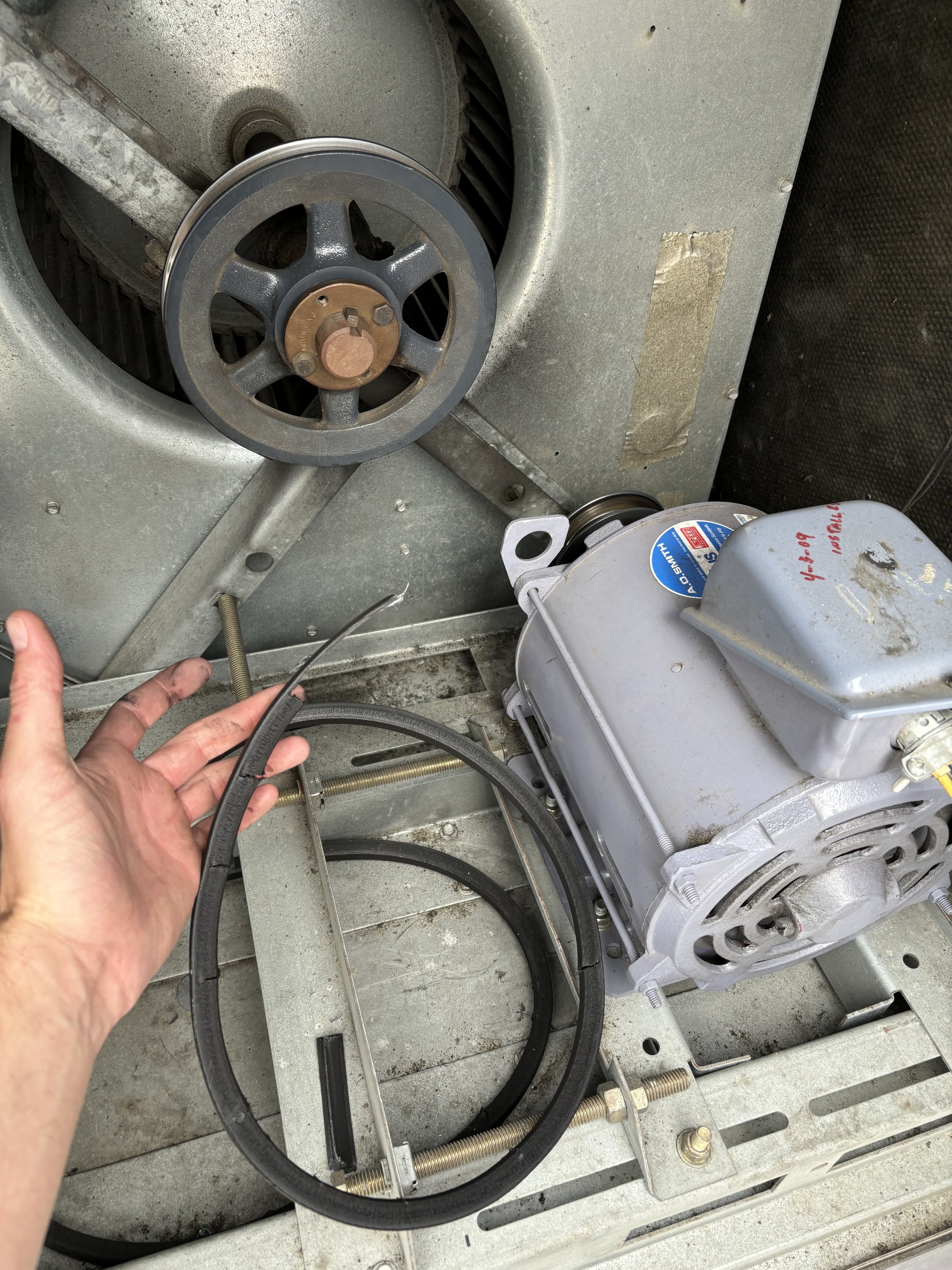 Close-up of an industrial machine part with a hand holding a belt and other mechanical components.