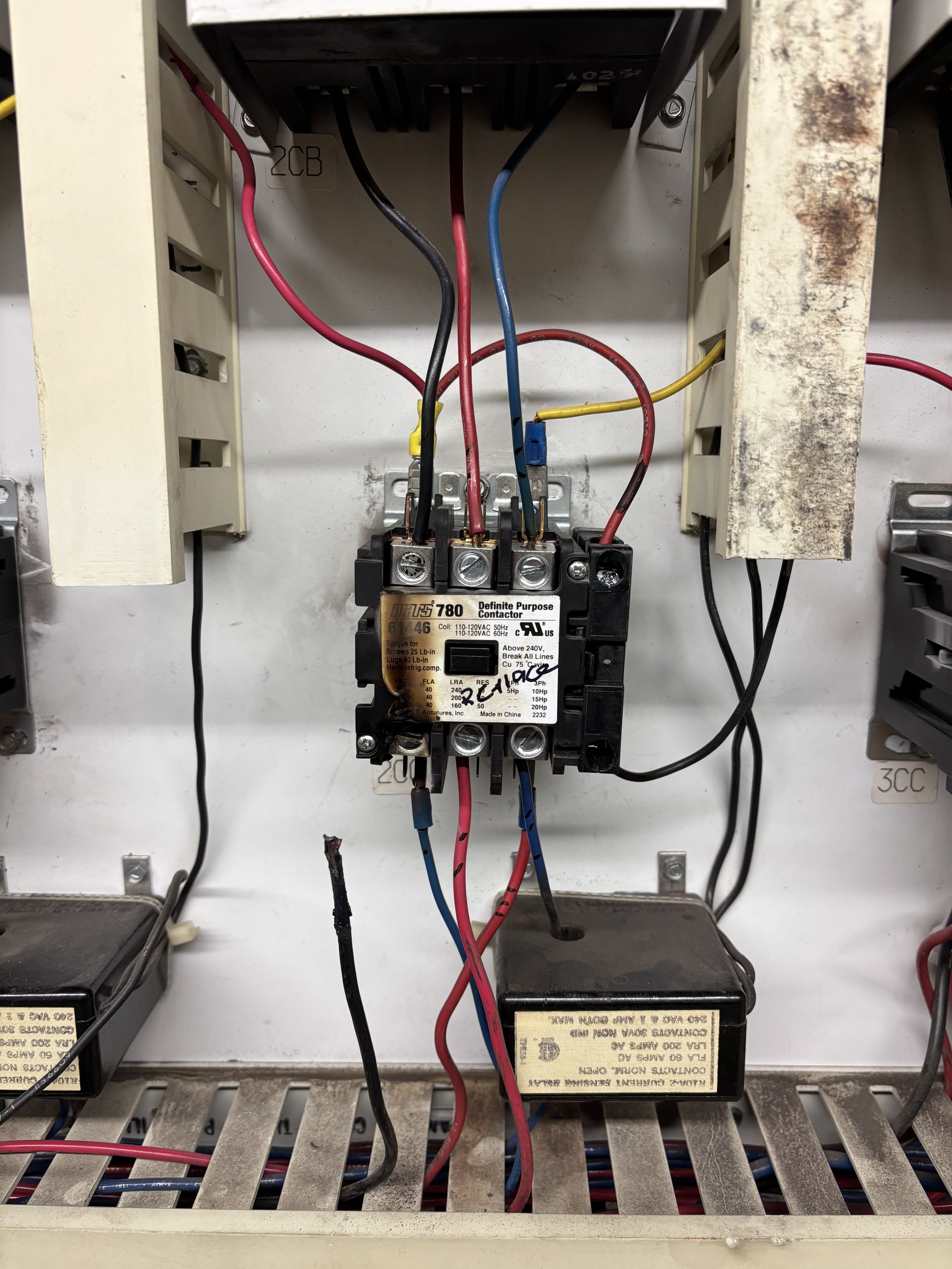 Inside an electrical panel, several colored wires connected to a black relay switch, with metal and plastic housing, some labels, and signs of usage or wear.