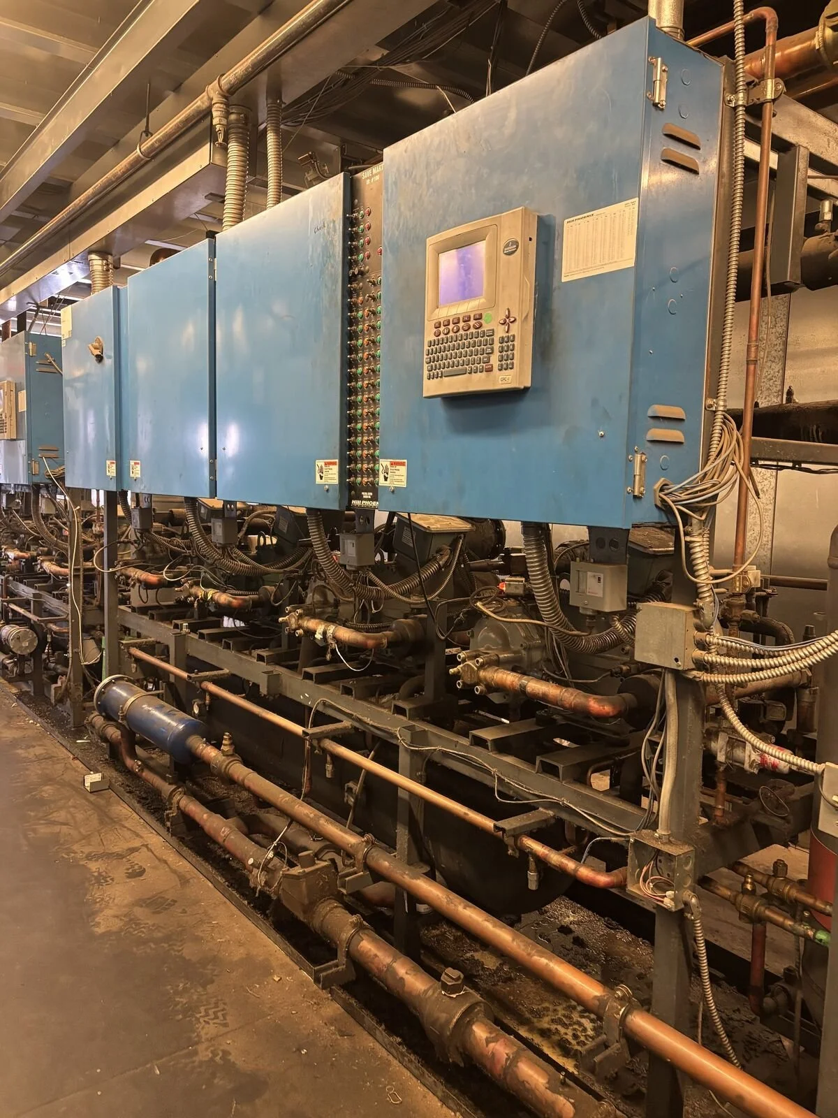 Industrial equipment with blue electrical boxes, pipes, and wiring in a factory or utility room.