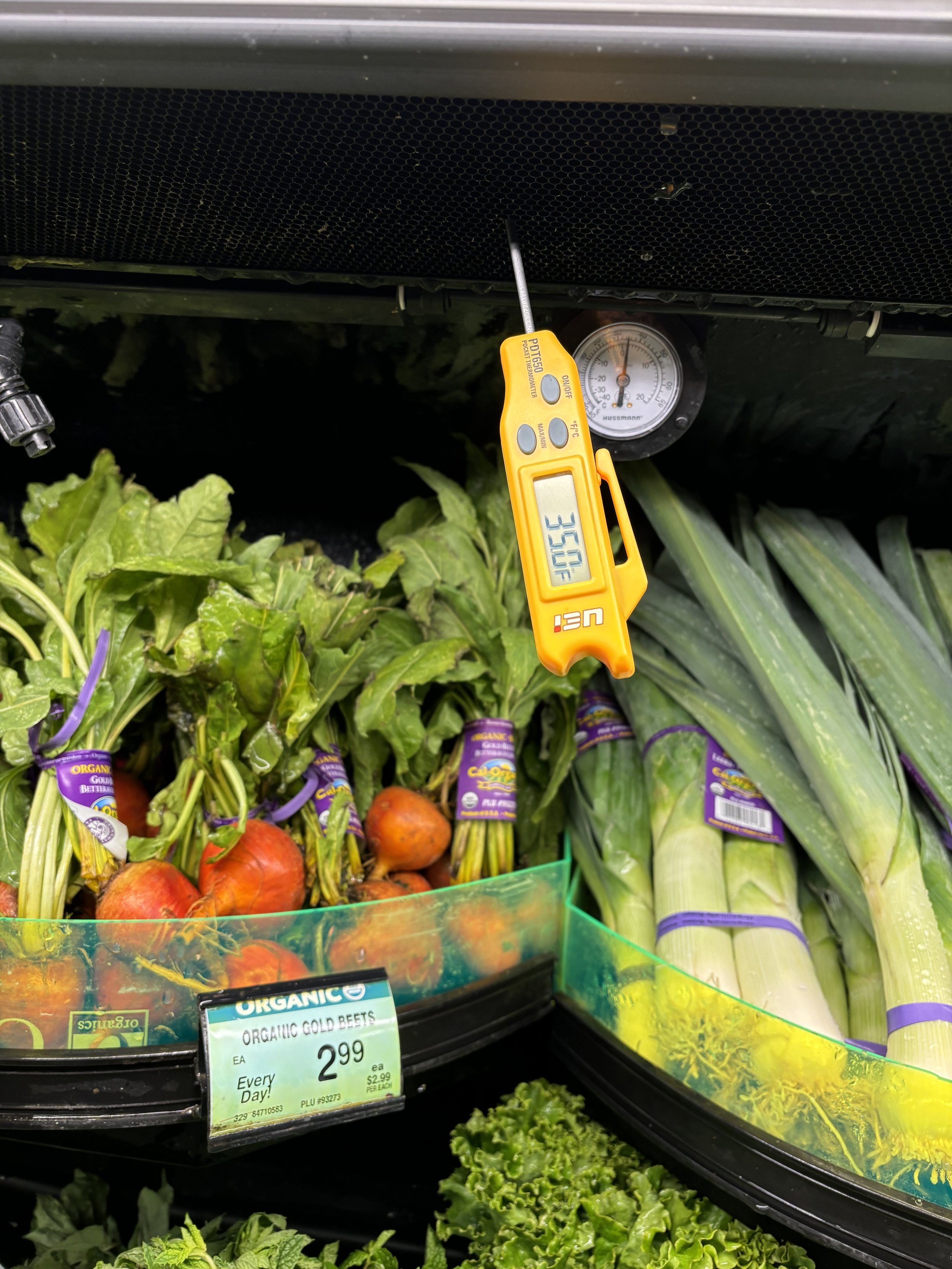 Fresh vegetables on display at a grocery store, including gold beets and leafy greens, with a digital thermometer showing a temperature of 35.0°F.