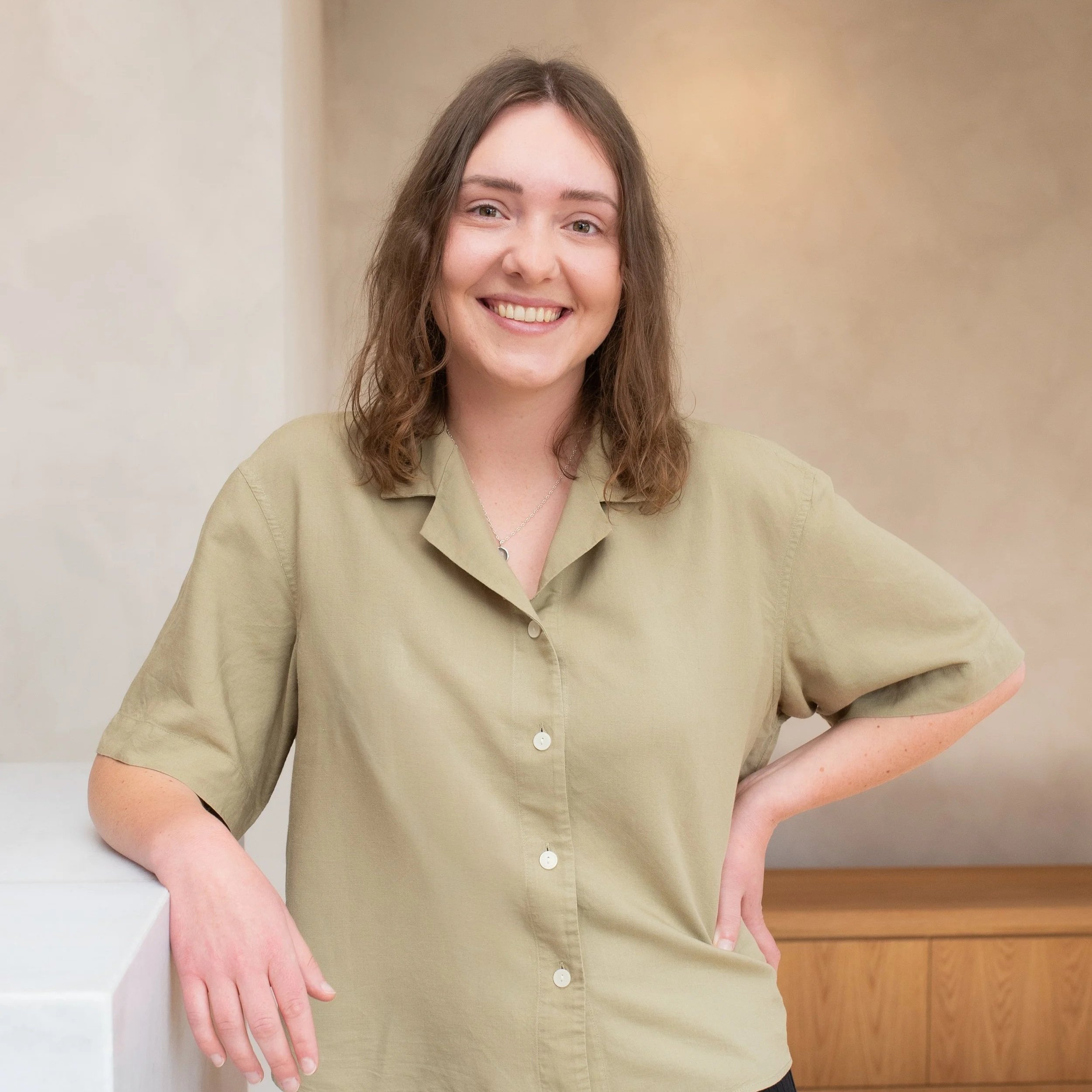 A young woman with brown hair smiling, wearing a light green shirt, against a plain light background.