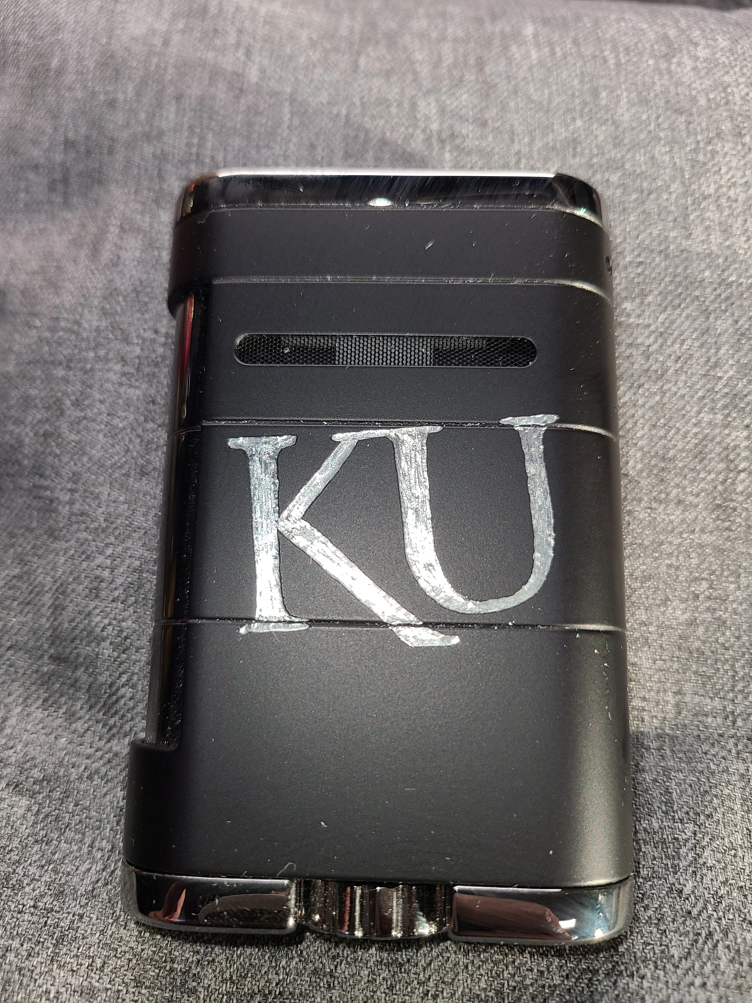 Close-up of a black lighter with a silver letter 'K' and 'U' engraved on the front