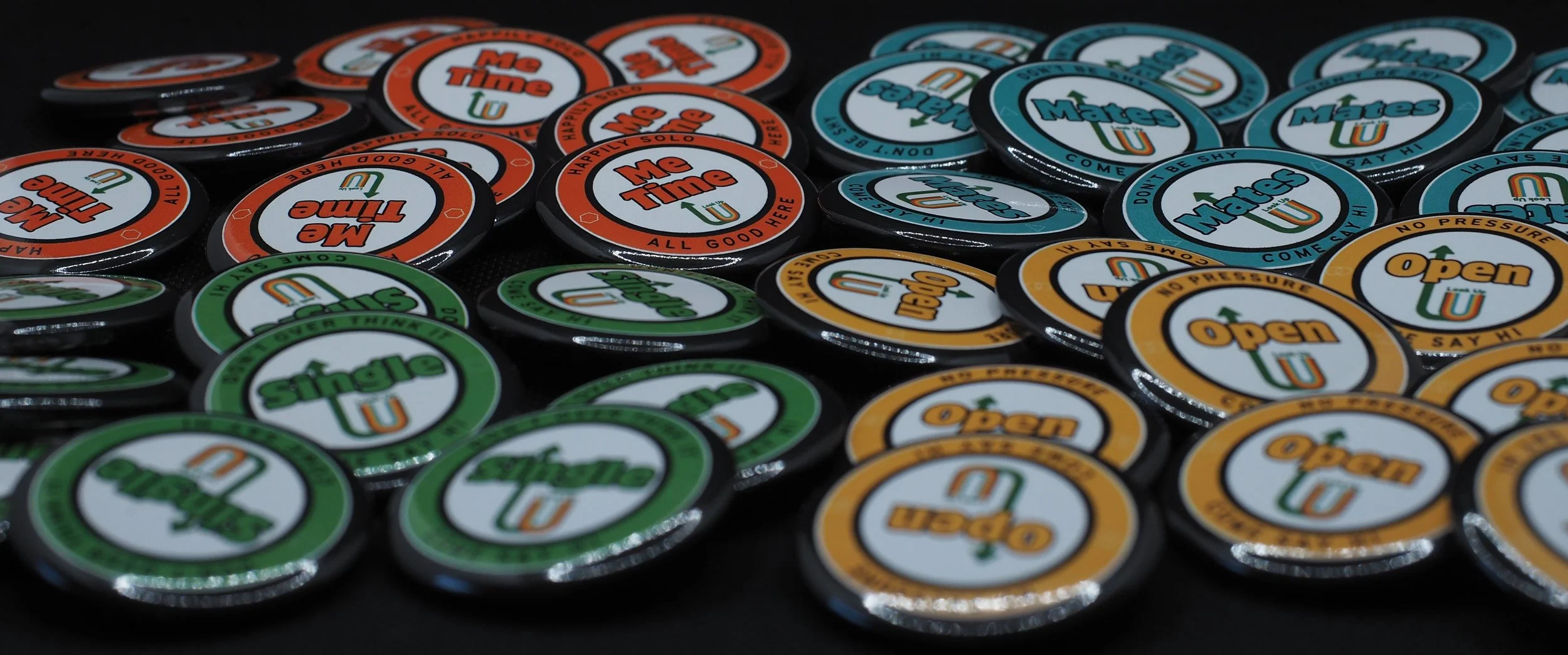 Collection of circular tokens in red, green, yellow, blue, and black with various words like 'Me Time,' 'Mates U,' and 'Open' printed on them.