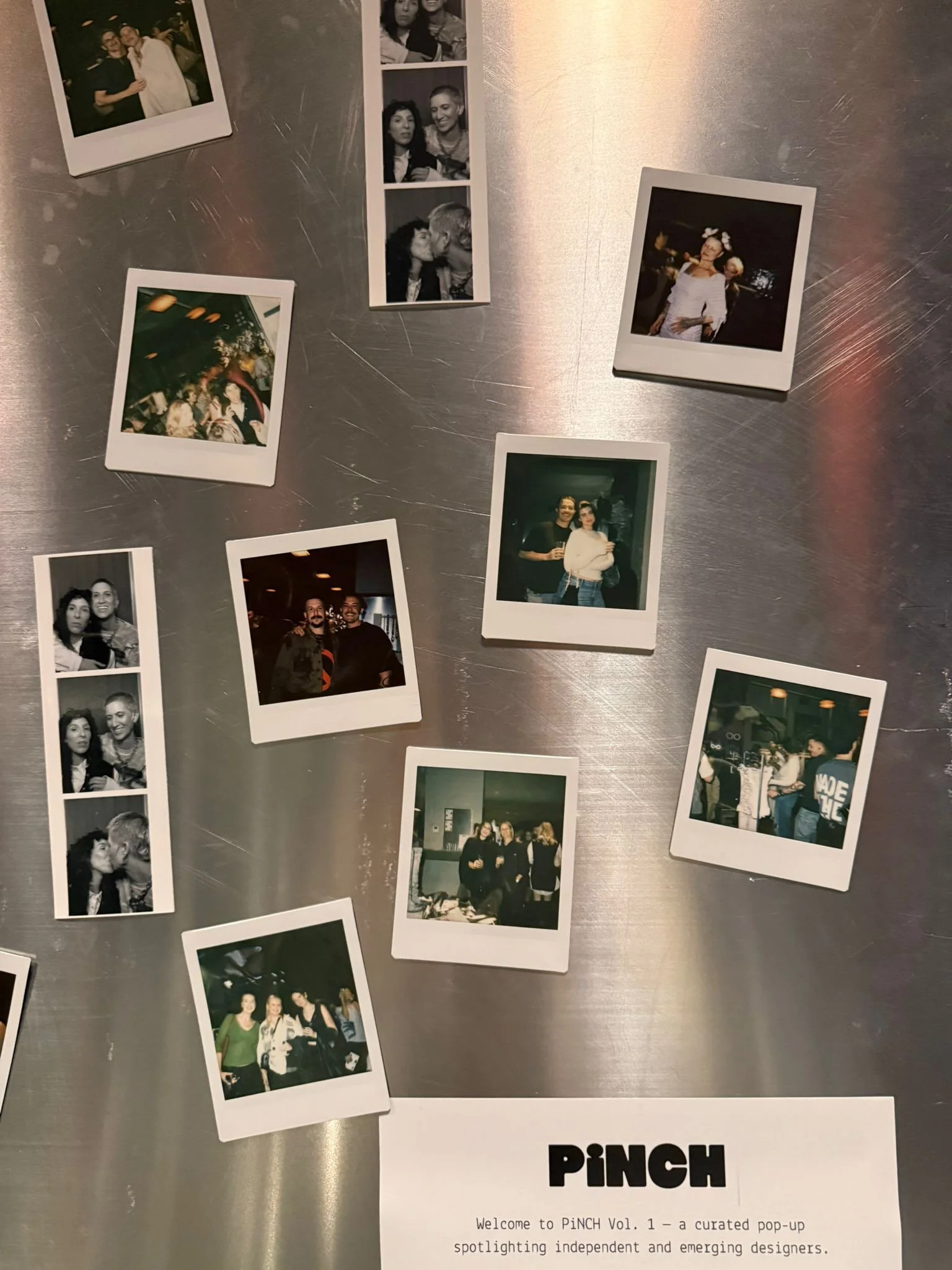 Arranged on a metallic surface are several Polaroid photos featuring groups of people at various social events, along with a printed page titled 'PINCH' that introduces a curated pop-up spotlighting independent and emerging designers.