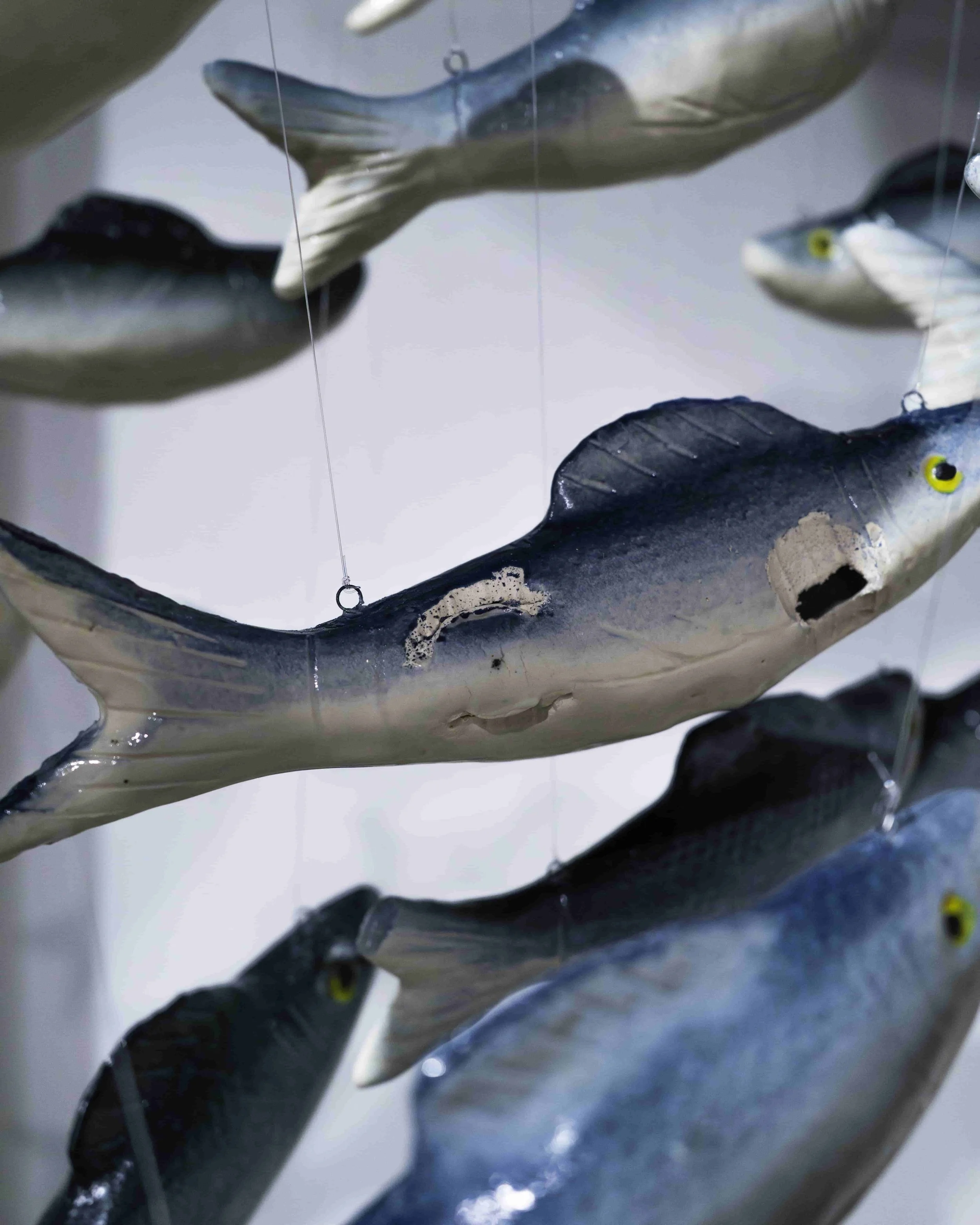 Close-up of colorful fish sculptures hanging from wires, with a rocky base underneath, created with painted and crafted materials.