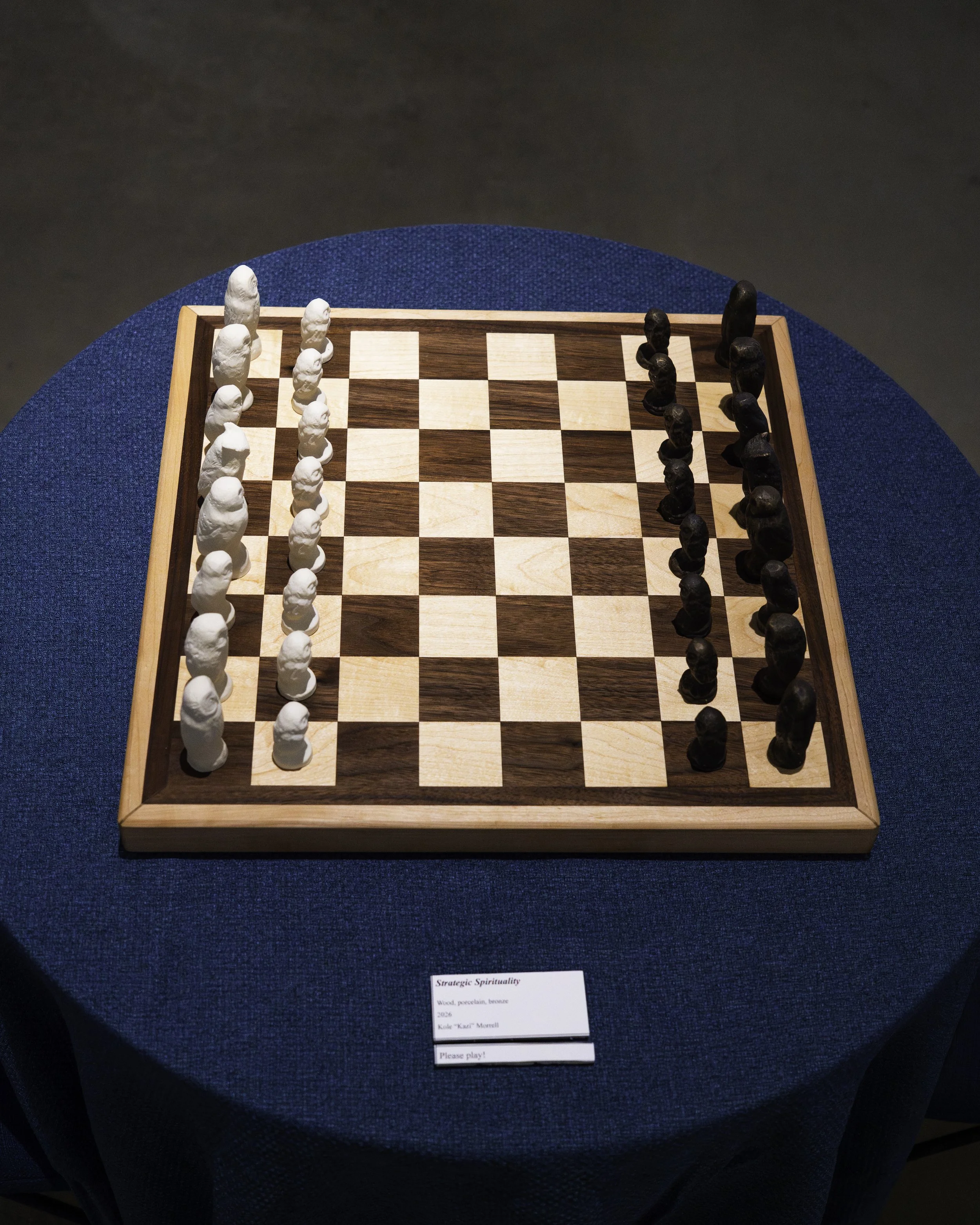 A chessboard with white and black pieces set up for a game, displayed on a blue table.
