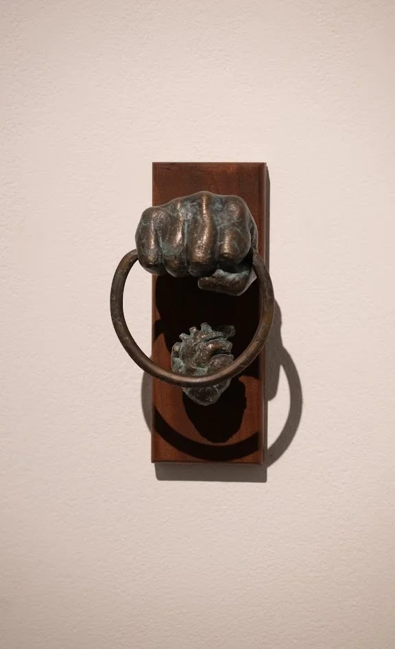 A sculpture of a hand gripping a door knocker on a wooden plaque.