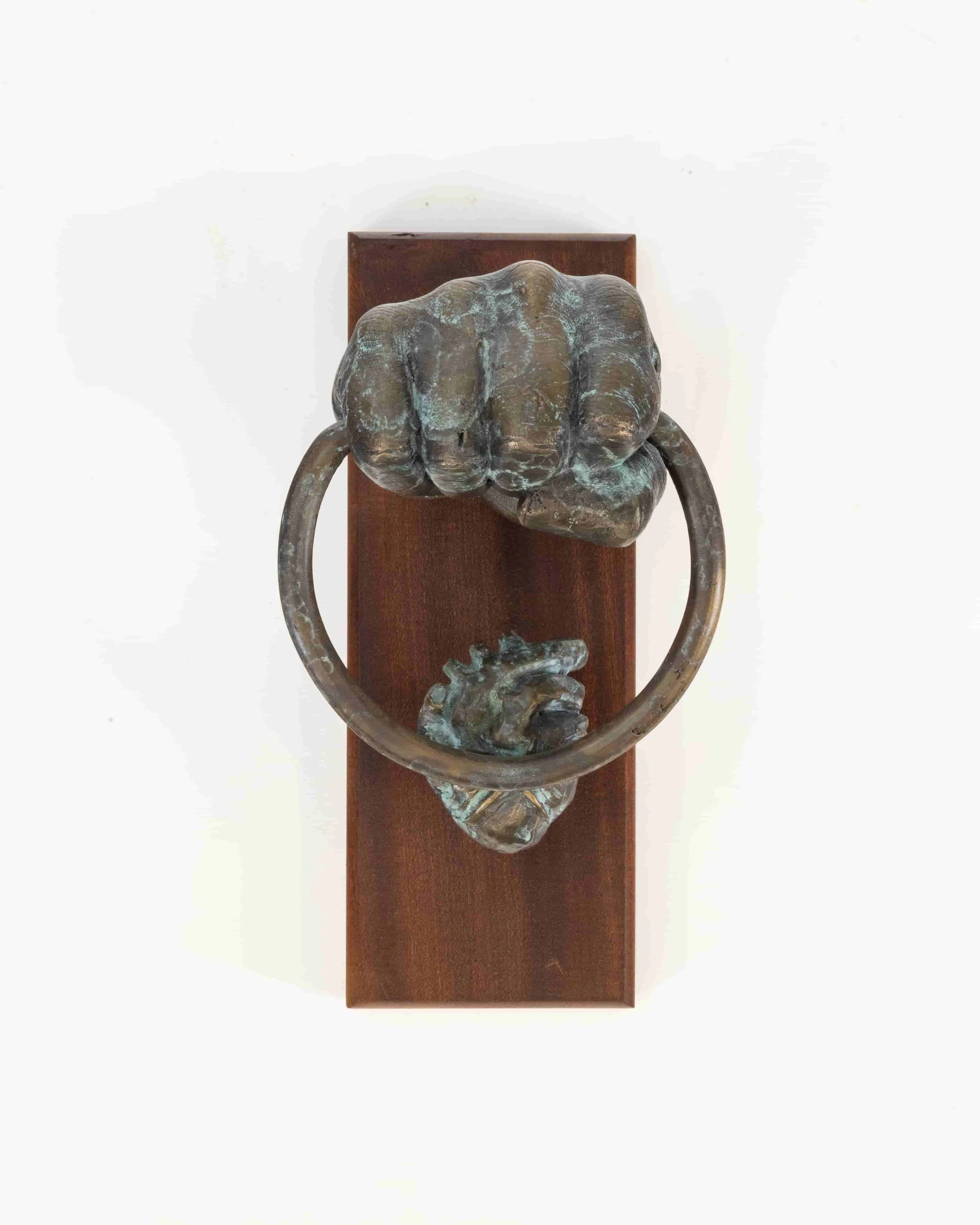 Bronze-colored sculpture of a fist gripping a circular ring, mounted on a wooden panel