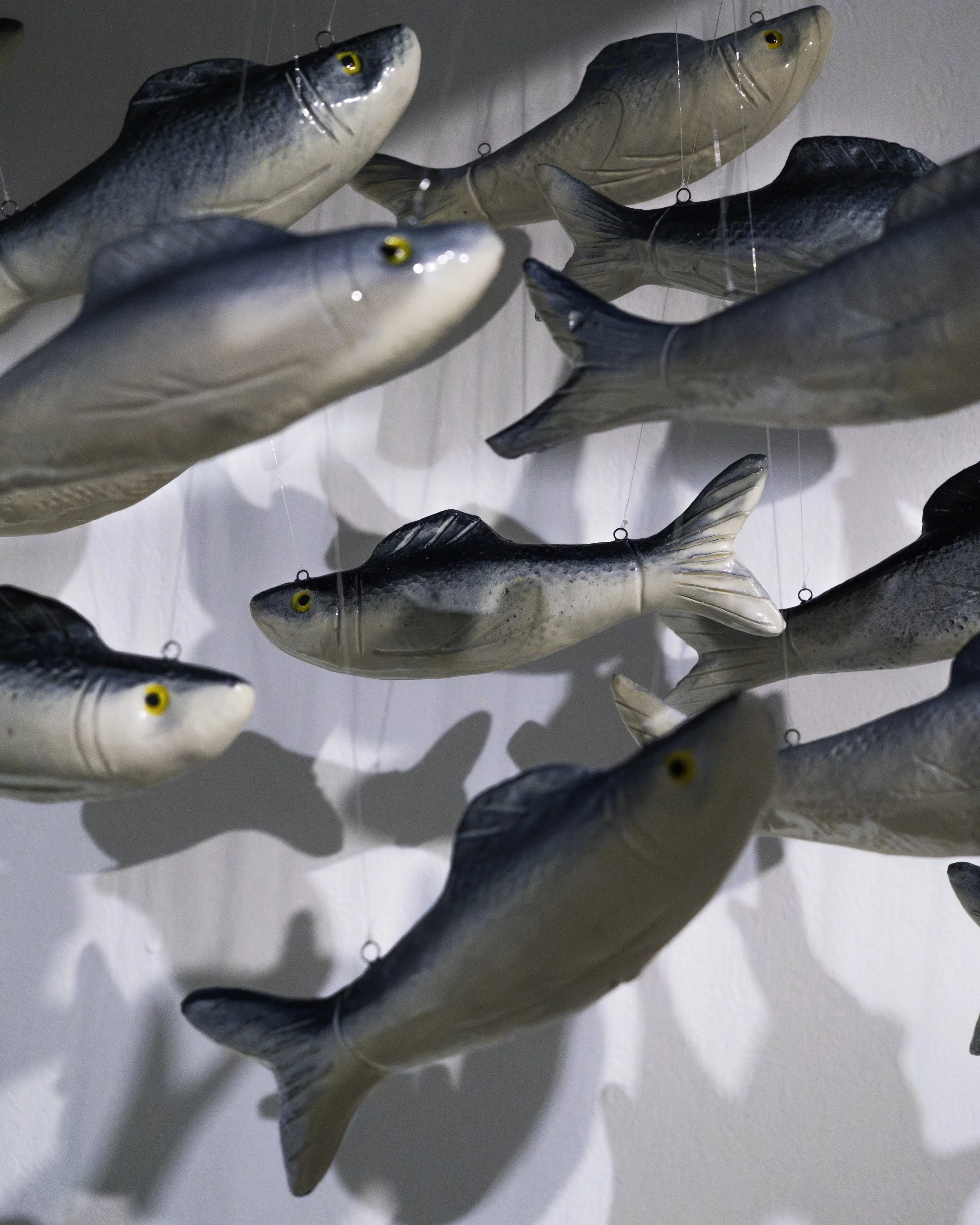 Multiple decorative fish-shaped items hanging on strings against a white wall.