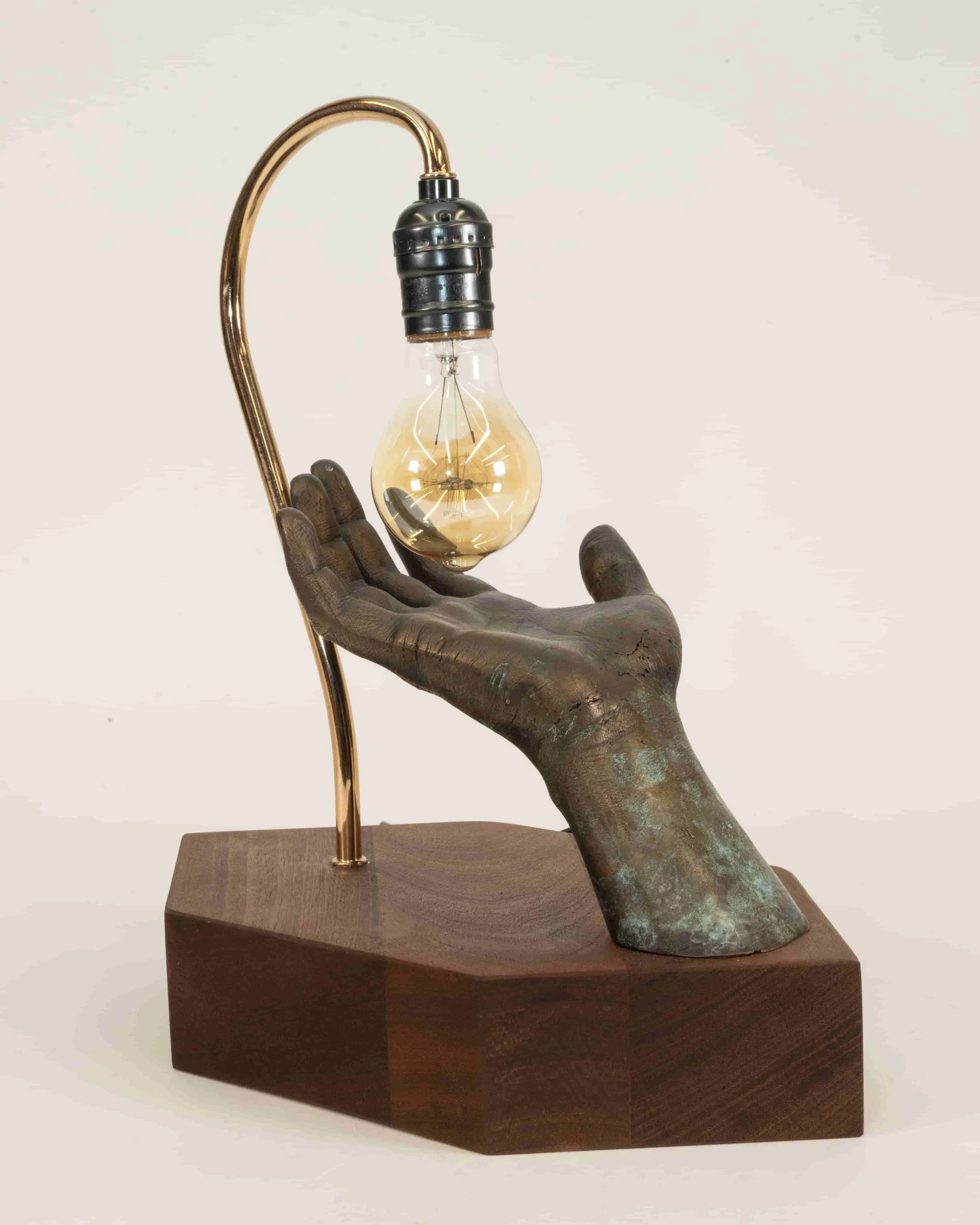 A decorative lamp with a hand-shaped base, holding a vintage-style light bulb, mounted on a wooden stand.