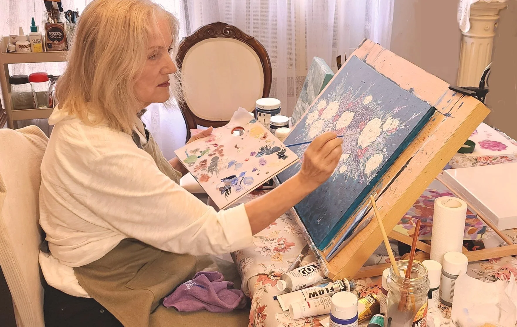 Artist Lauree Lindsay painting a floral scene on a canvas in an art studio.