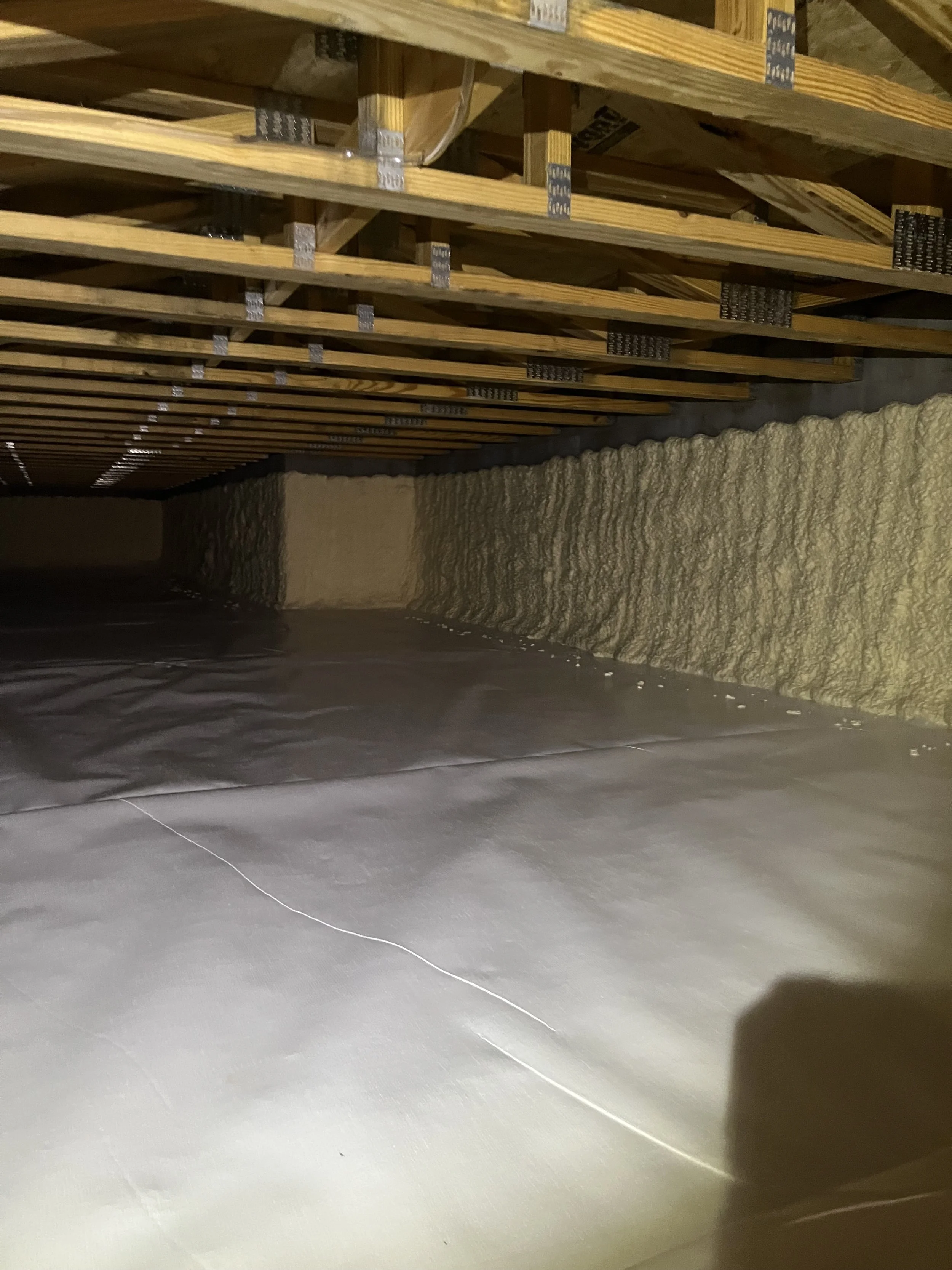 Insulation foam in a partially constructed basement ceiling with wooden framing and metal connectors.