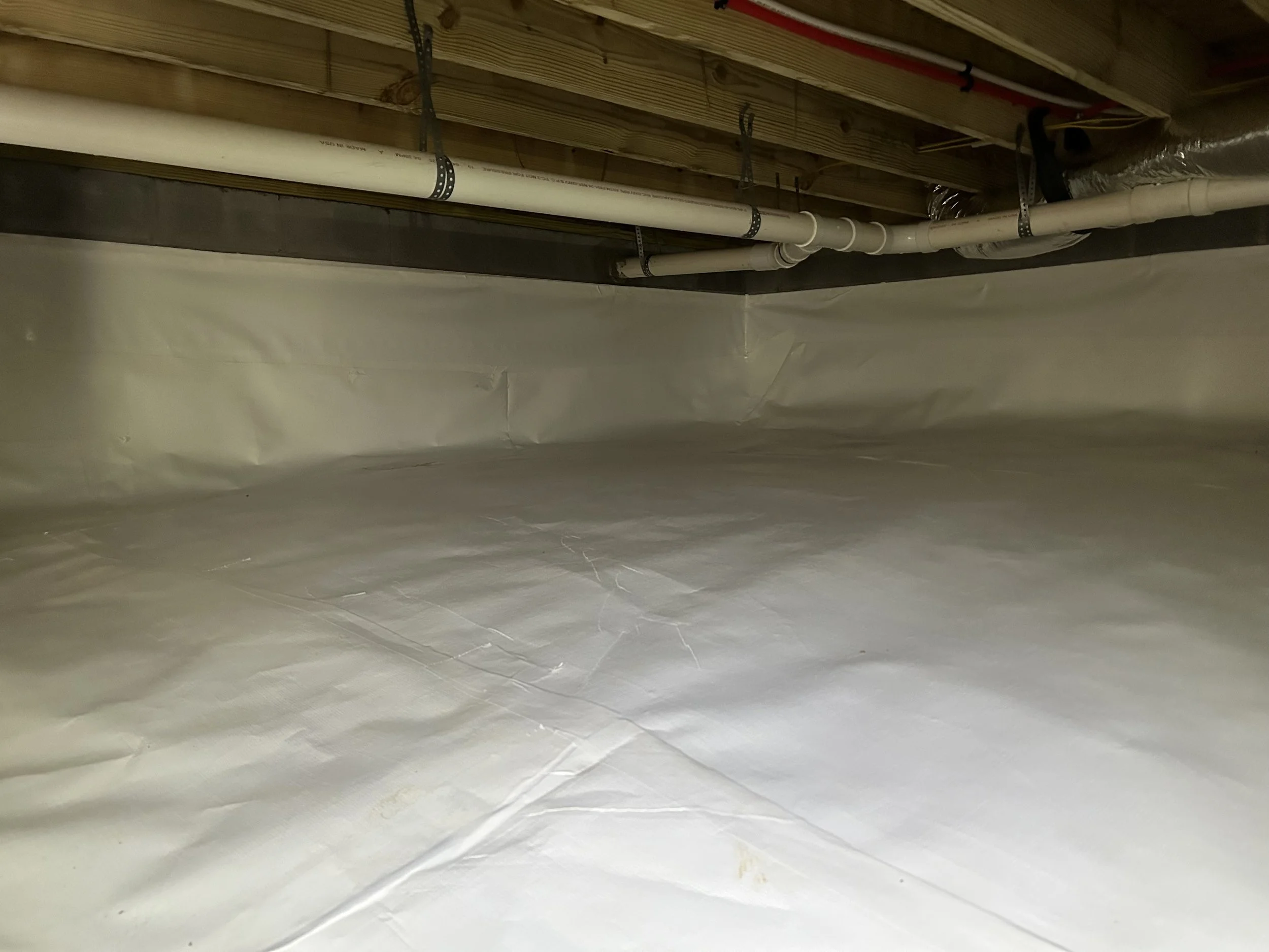 A view of an unfinished basement ceiling showing exposed wooden joists, pipes, and ductwork.
