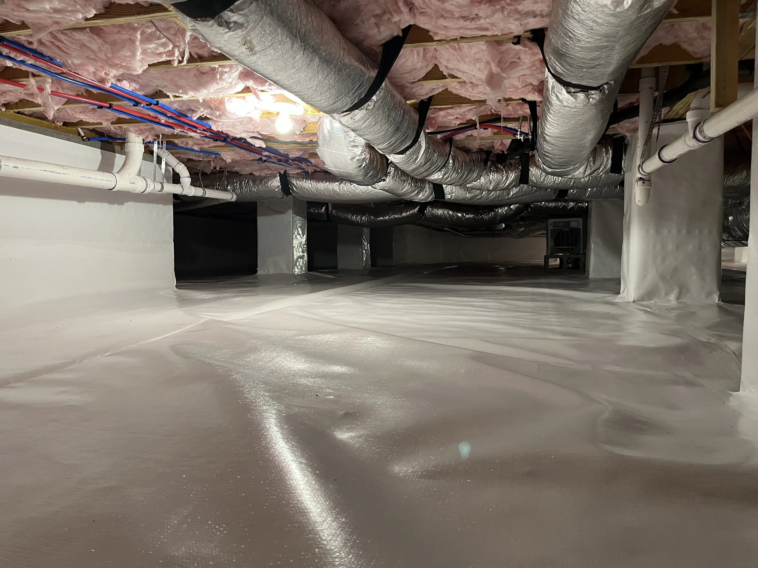 View of an unfinished basement ceiling with exposed ductwork, pipes, wiring, pink insulation, and wooden beams.