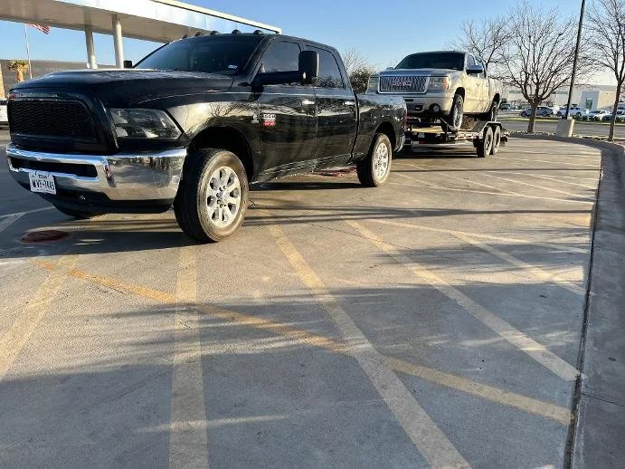 A black pickup truck towing a silver car on a trailer in a parking lot with empty spaces.