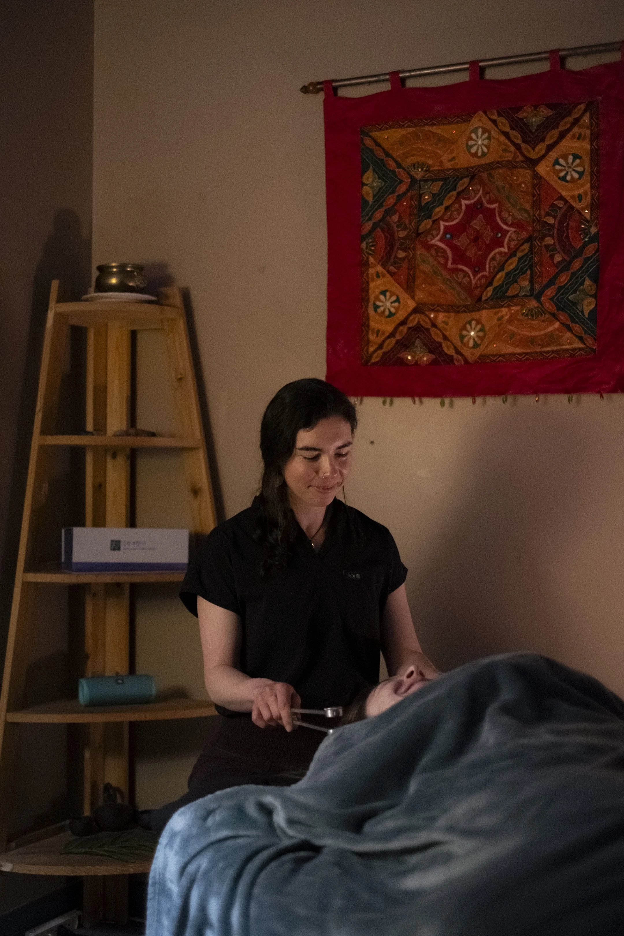 A practitioner uses weighted tuning forks in a sound healing treatment to support relaxation and balance during a treatment session.