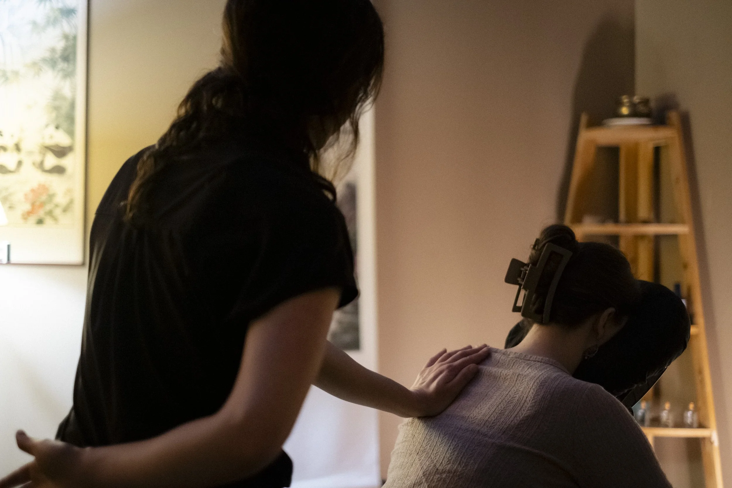 A massage therapist massages a client’s upper back during a seated chair massage.