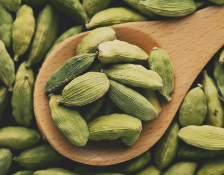 Fresh green cardamom pods on a wooden spoon and surrounding surface.