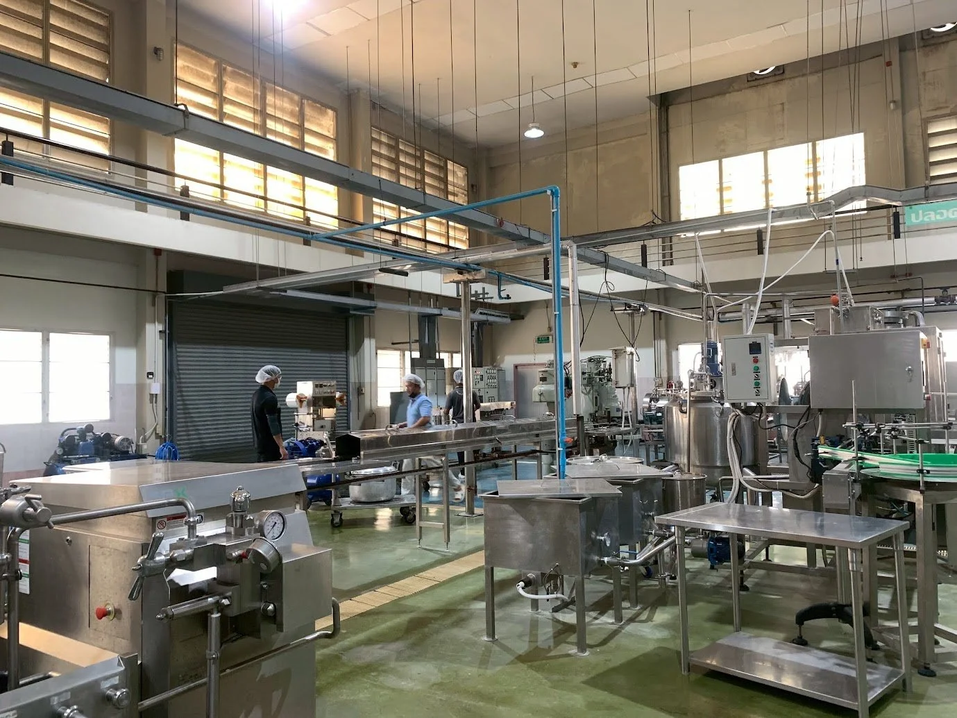 Industrial food processing or manufacturing facility with stainless steel equipment, conveyor belts, and workers wearing hairnets and protective clothing.