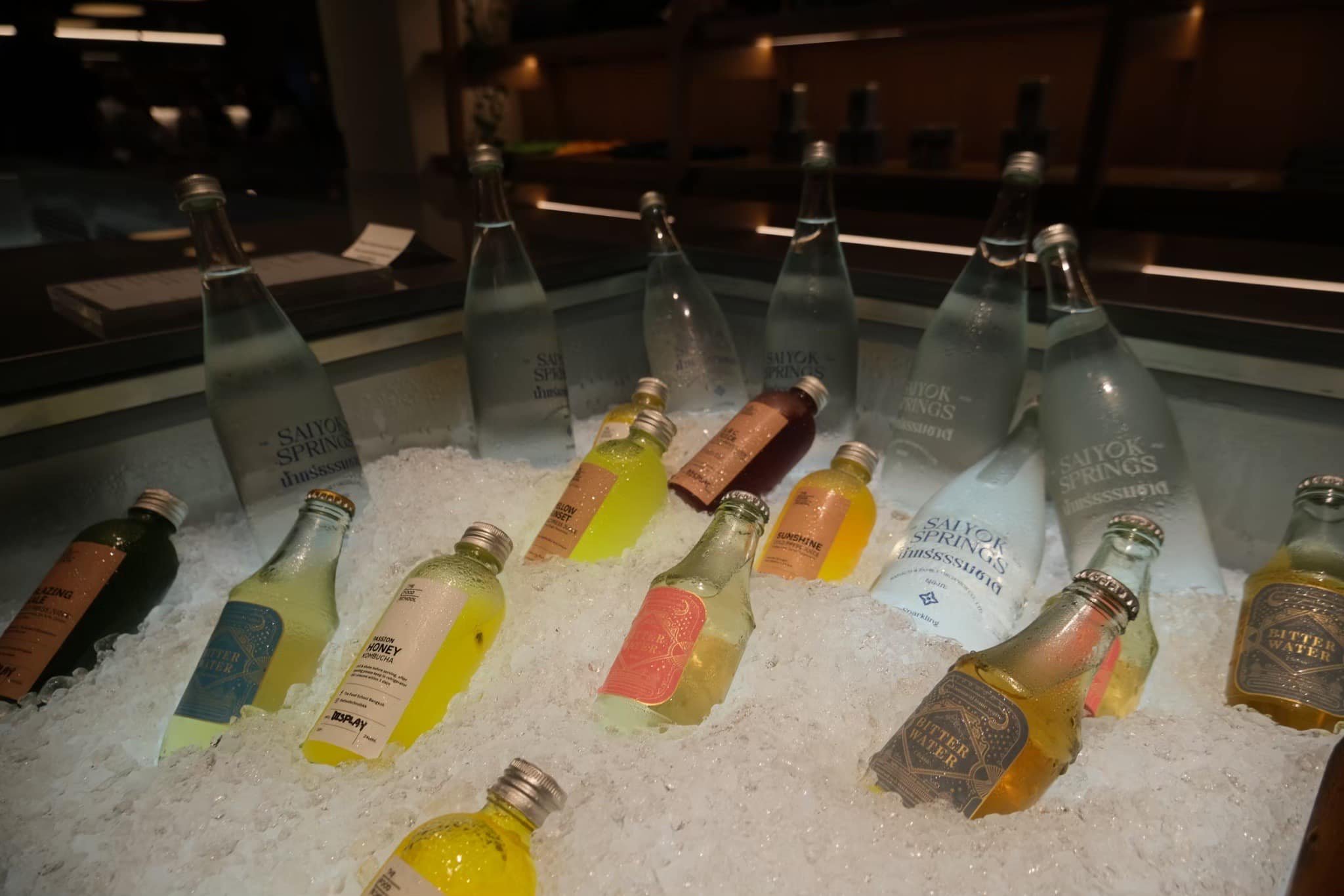 Several bottles of beverages, including sparkling water and flavored drinks, are placed on ice in a refrigerated display case at a bar or restaurant.