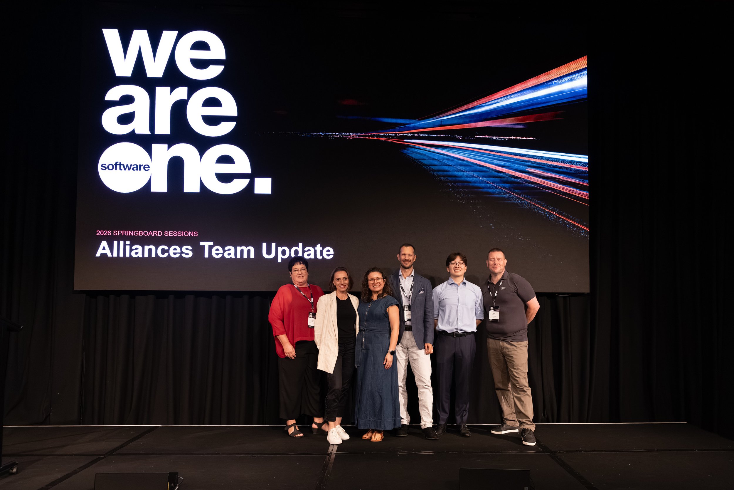 Group of six people standing on stage in front of a large screen with the words "We are one. software" and "Alliances Team Update."