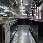Empty industrial kitchen with stainless steel countertops and appliances, fluorescent lighting, and large windows