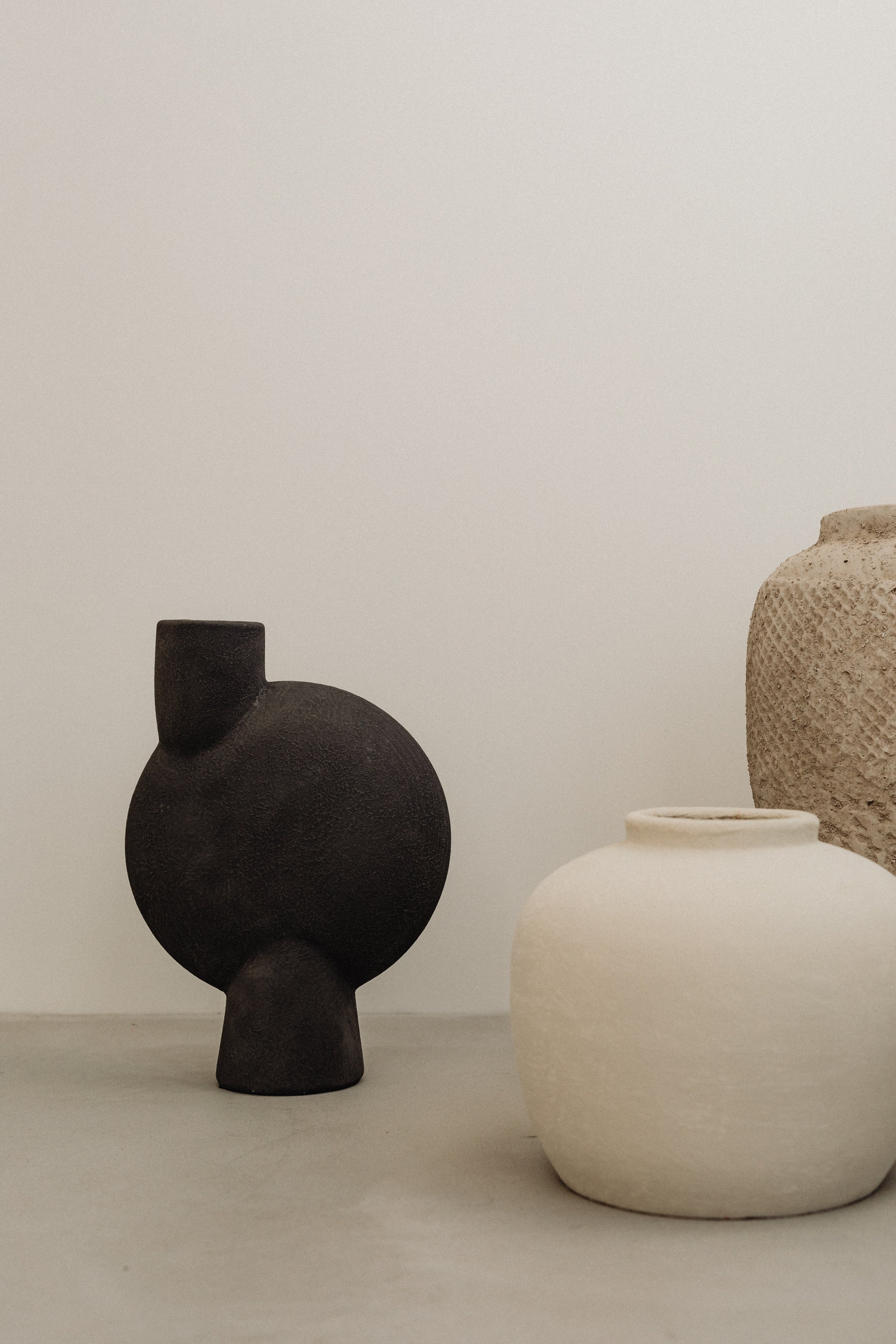 Four minimalist vases in black, white, and beige, with different textures and shapes, arranged on a surface against a plain background.