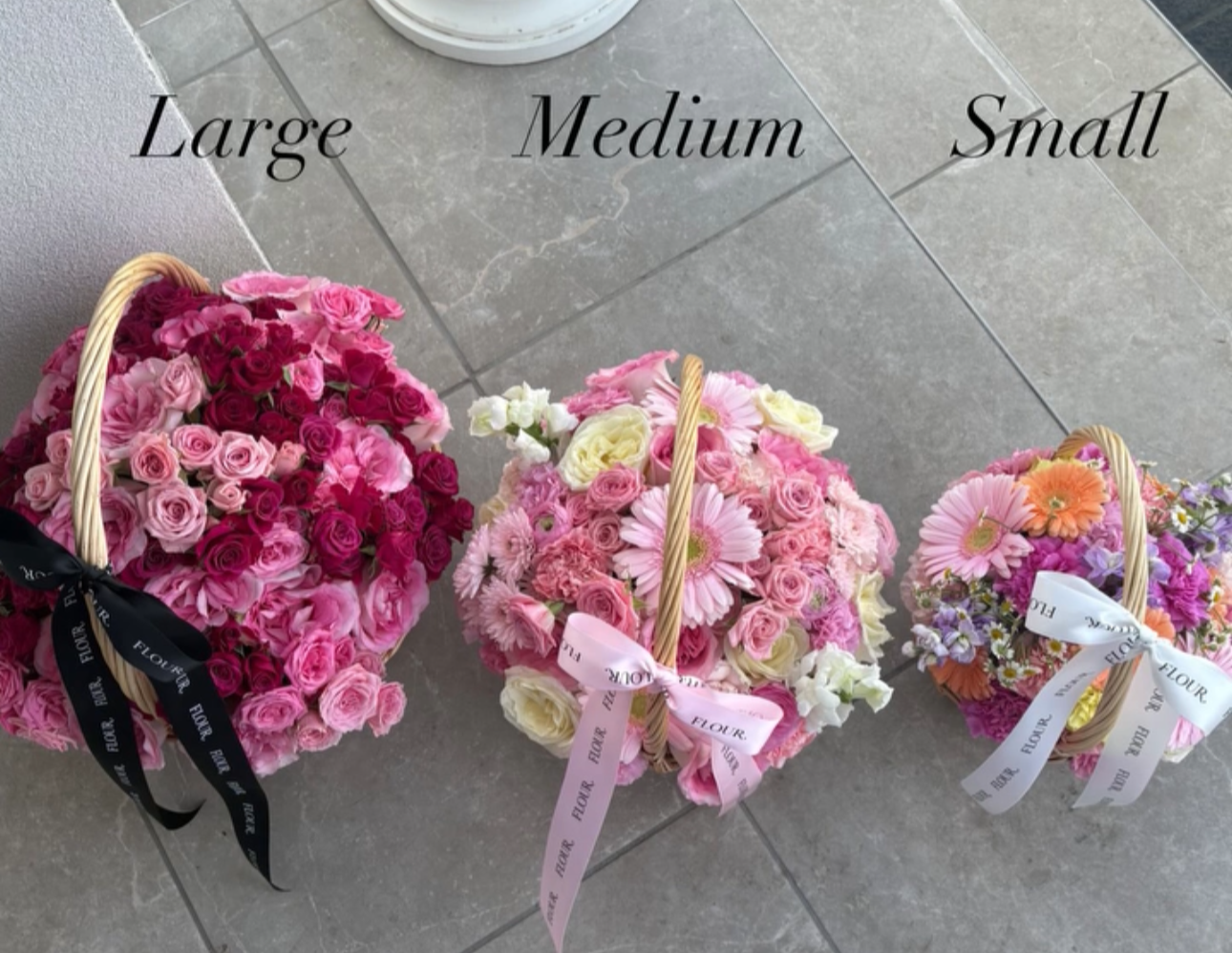 Three flower baskets labeled Large, Medium, and Small, filled with pink, white, and purple flowers, decorated with ribbons.