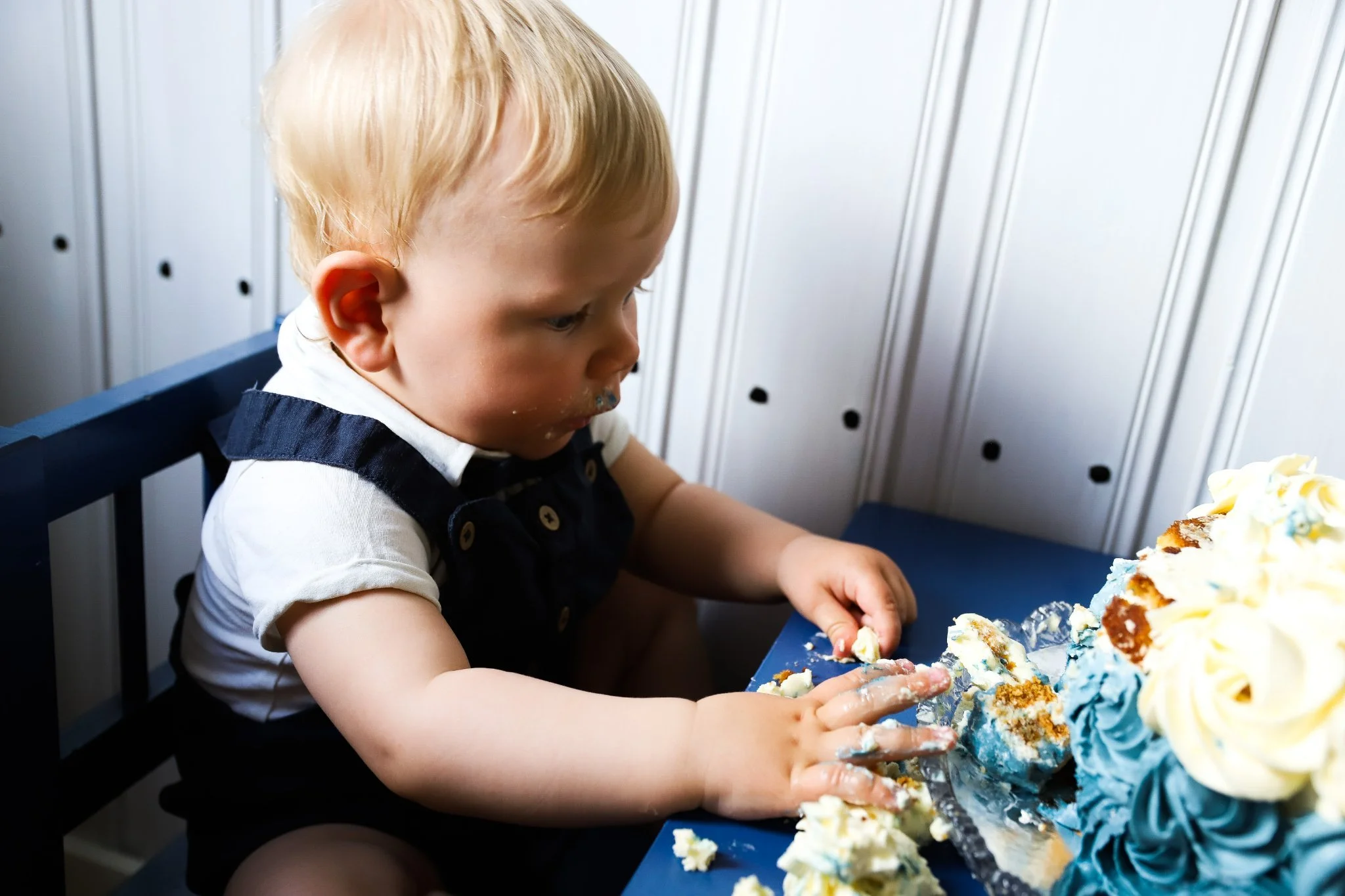 En ung pojke med blont hår som äter en tårta med blå och vit frosting.